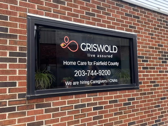 Brick exterior wall with a window sign advertising Griswold Home Care and job openings.