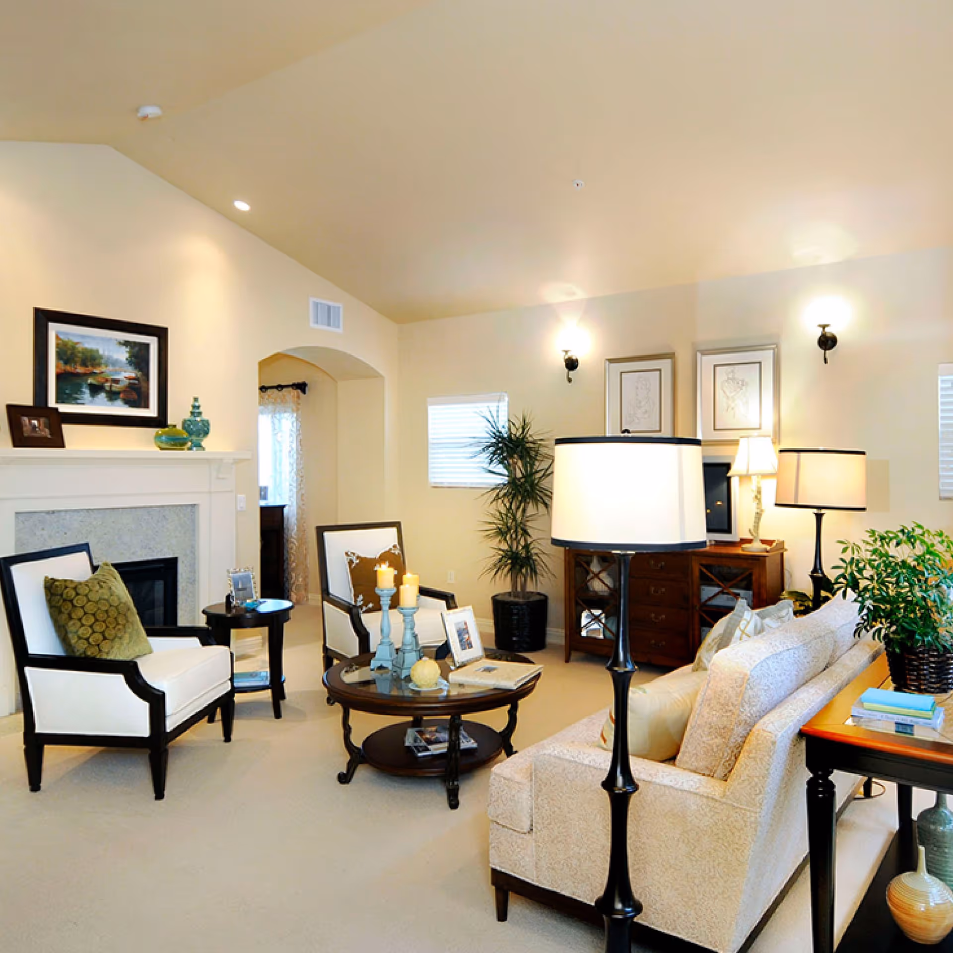 Bright, cozy living room with sofas, chairs, fireplace, and plants in a senior living facility.