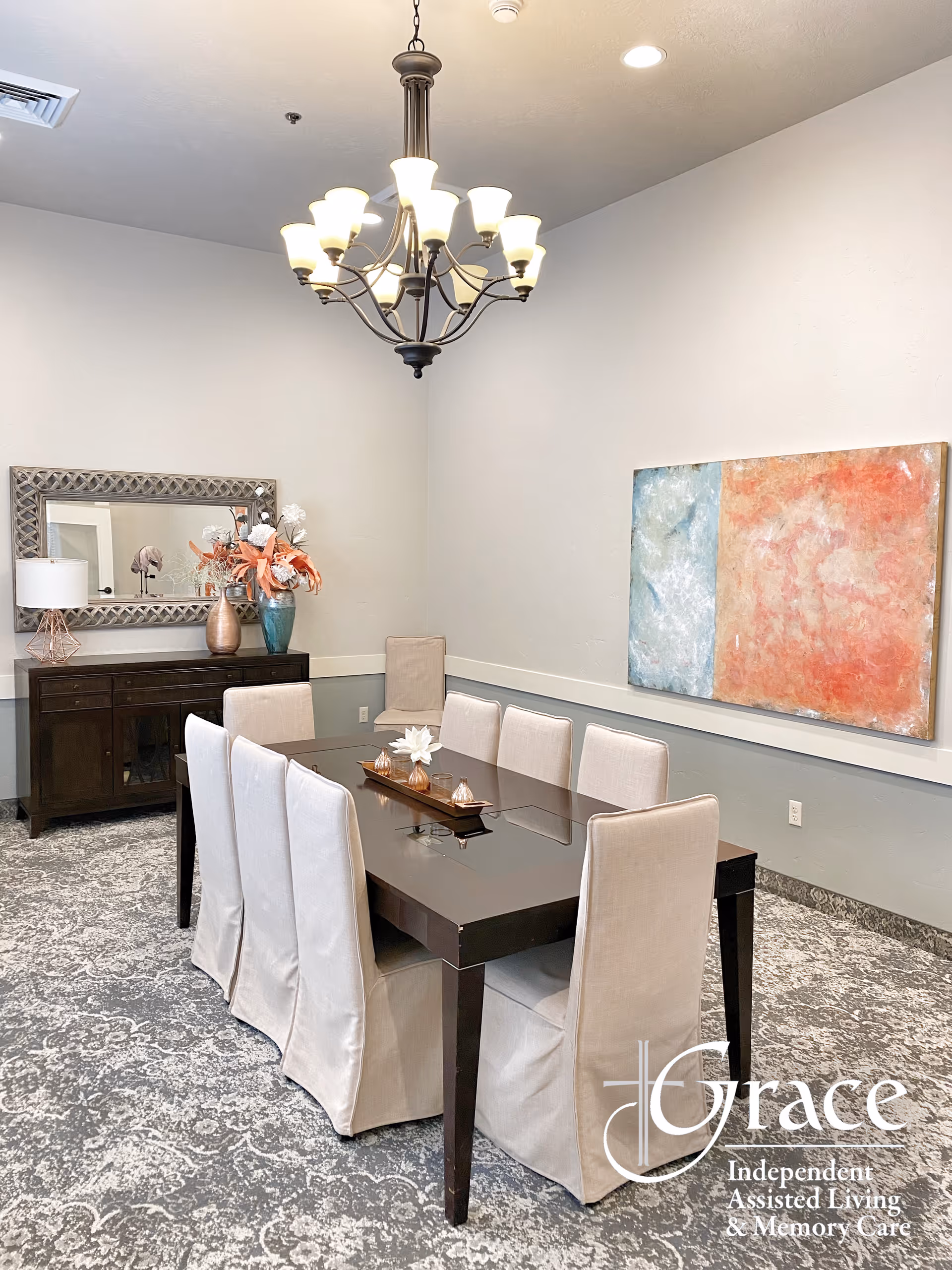 A formal dining room with a dark table, beige chairs, chandelier, and artwork.