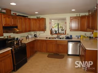 Large U-shaped kitchen with wooden cabinets, a black stove, stainless steel dishwasher, and a window above the sink.