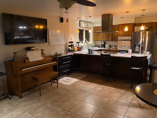 Open kitchen with island, bar stools, cabinets, appliances, and a piano against the wall.