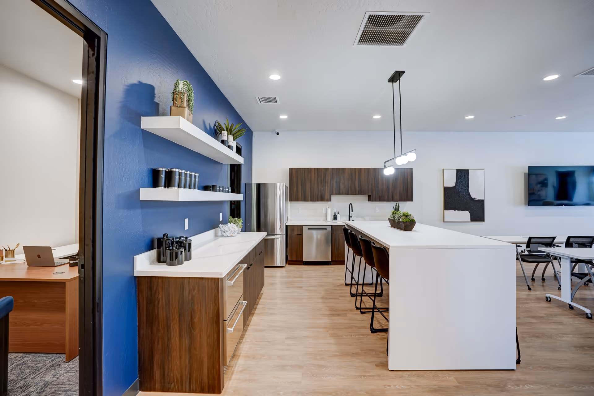 Modern communal kitchen with a white island, blue wall, and stainless steel appliances.