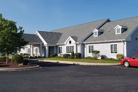 Front exterior of a single-story annex building with a gabled roof, entrance portico, shrubs, and an adjacent parking lot.