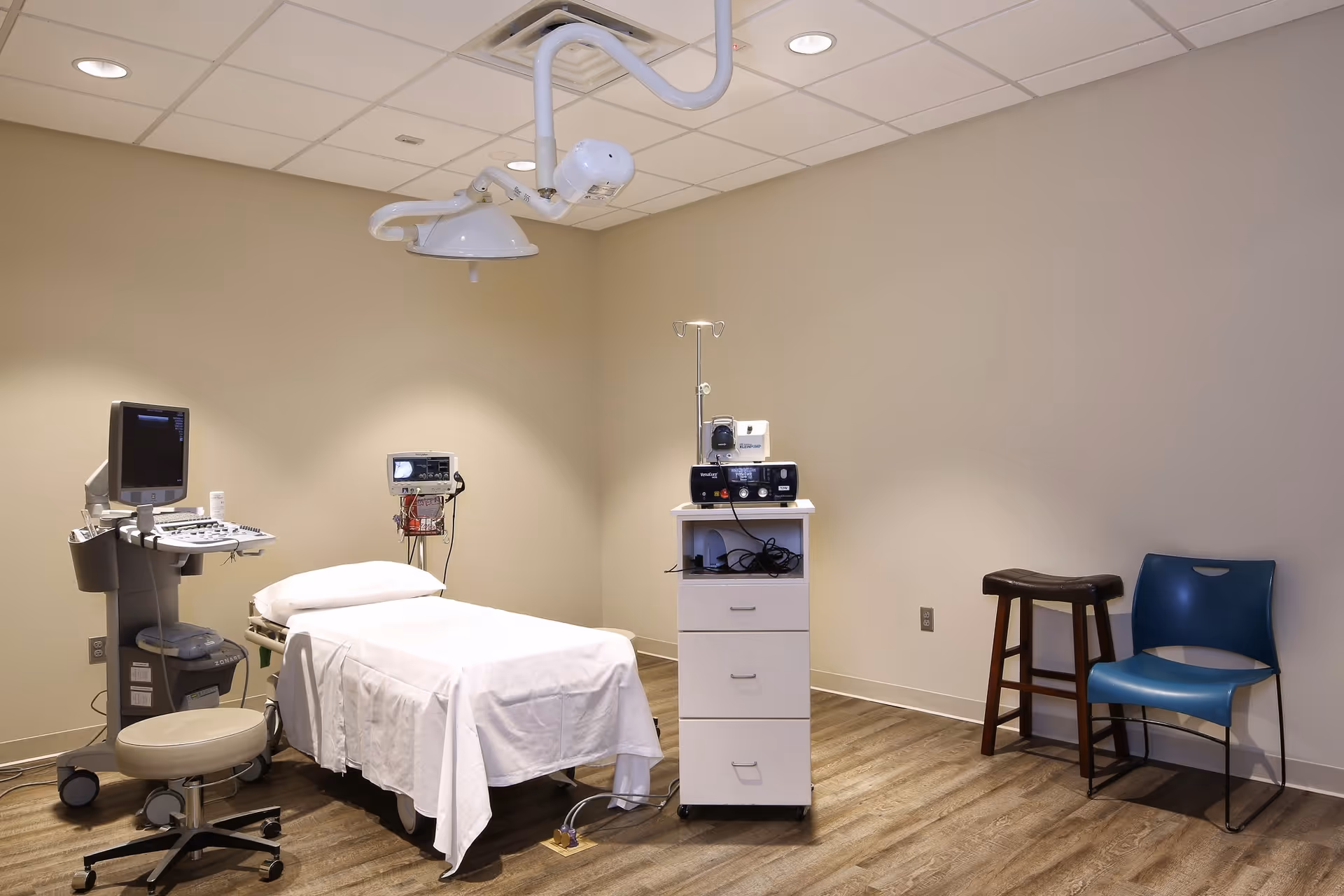 Medical examination room with a treatment bed, monitors, IV pole, and medical equipment.