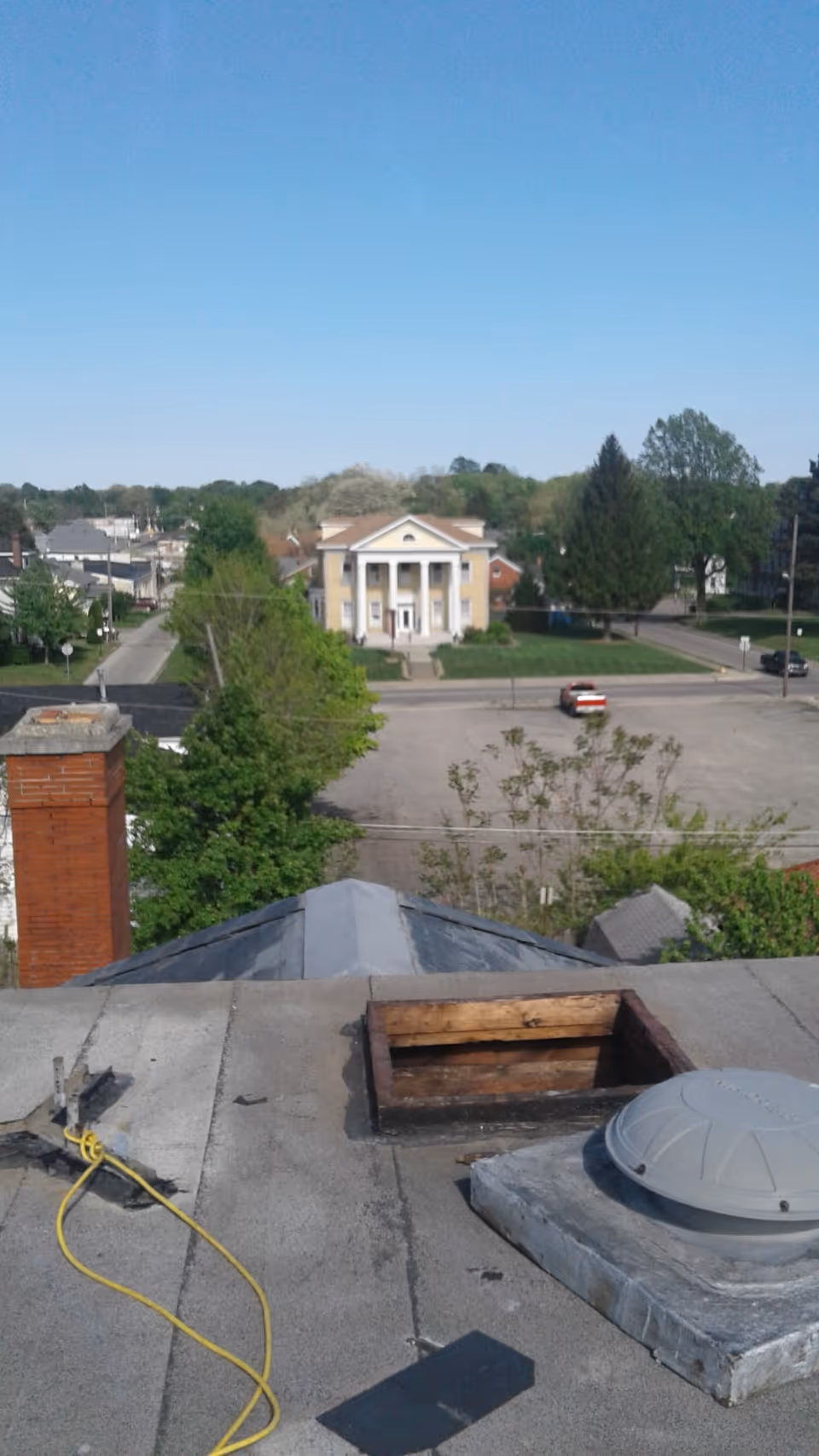 Rooftop view of a street with a yellow, columned building in the distance.
