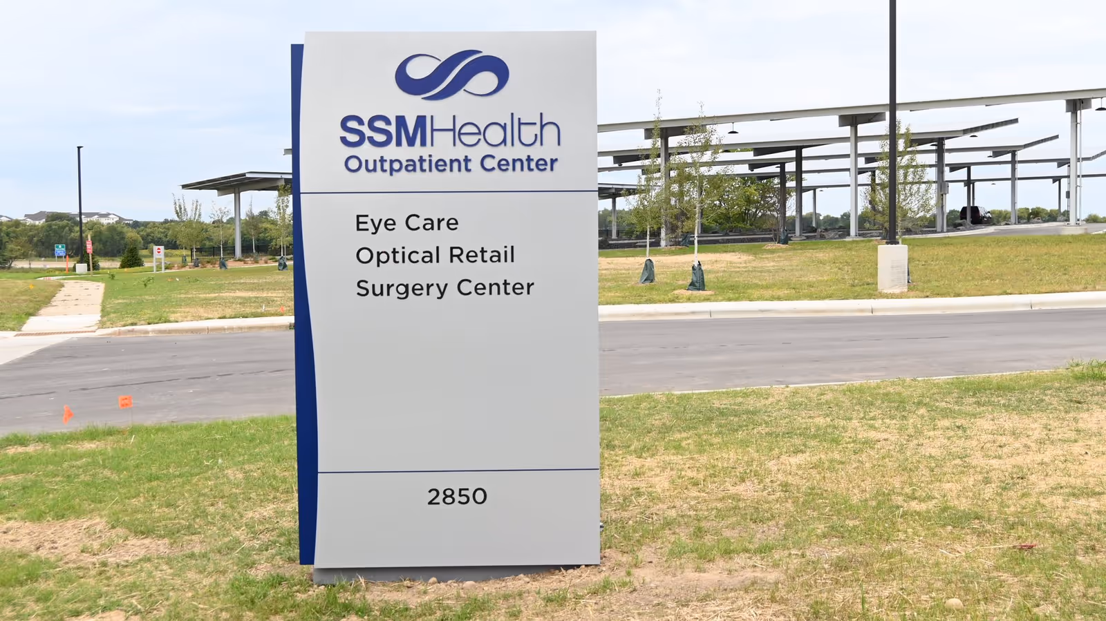 Large gray SSM Health Outpatient Center sign on grass near road and canopy structures.