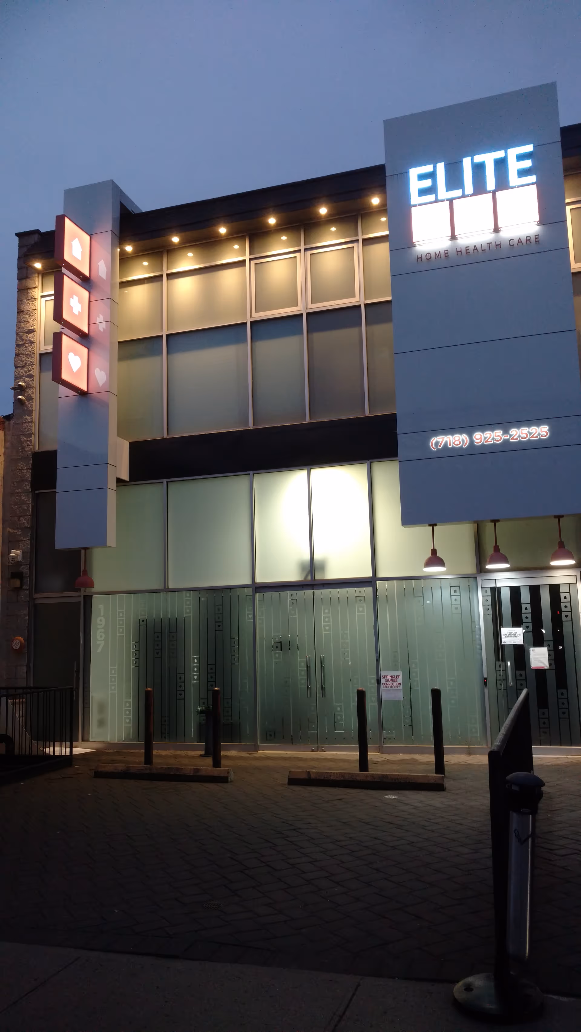 Front exterior of Elite Home Health Care building with illuminated sign and glass windows at dusk.