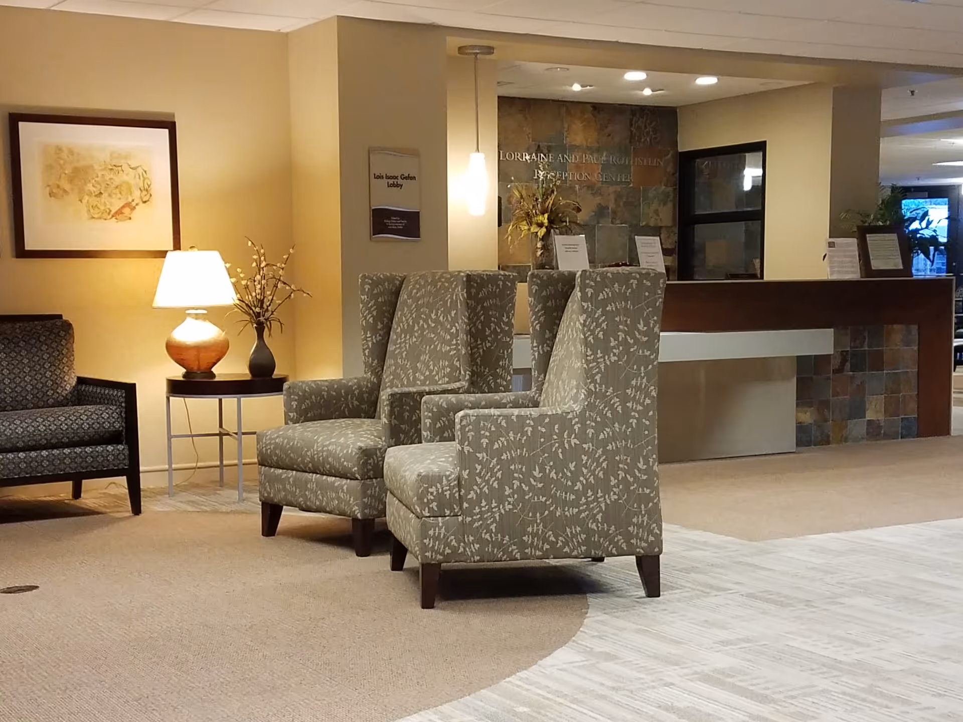 Interior lobby area with patterned armchairs, a lamp, and a reception desk.