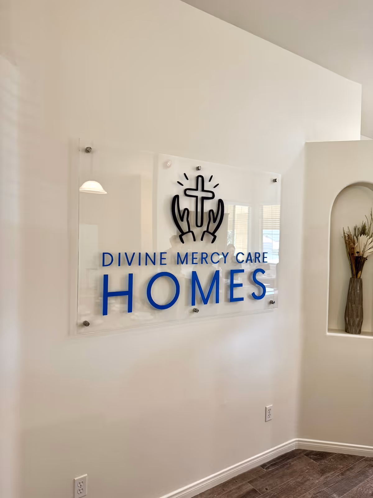 Interior wall sign reads Divine Mercy Care Homes with a cross logo.