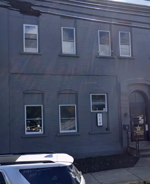 Grey brick building exterior with multiple windows and a parked car out front