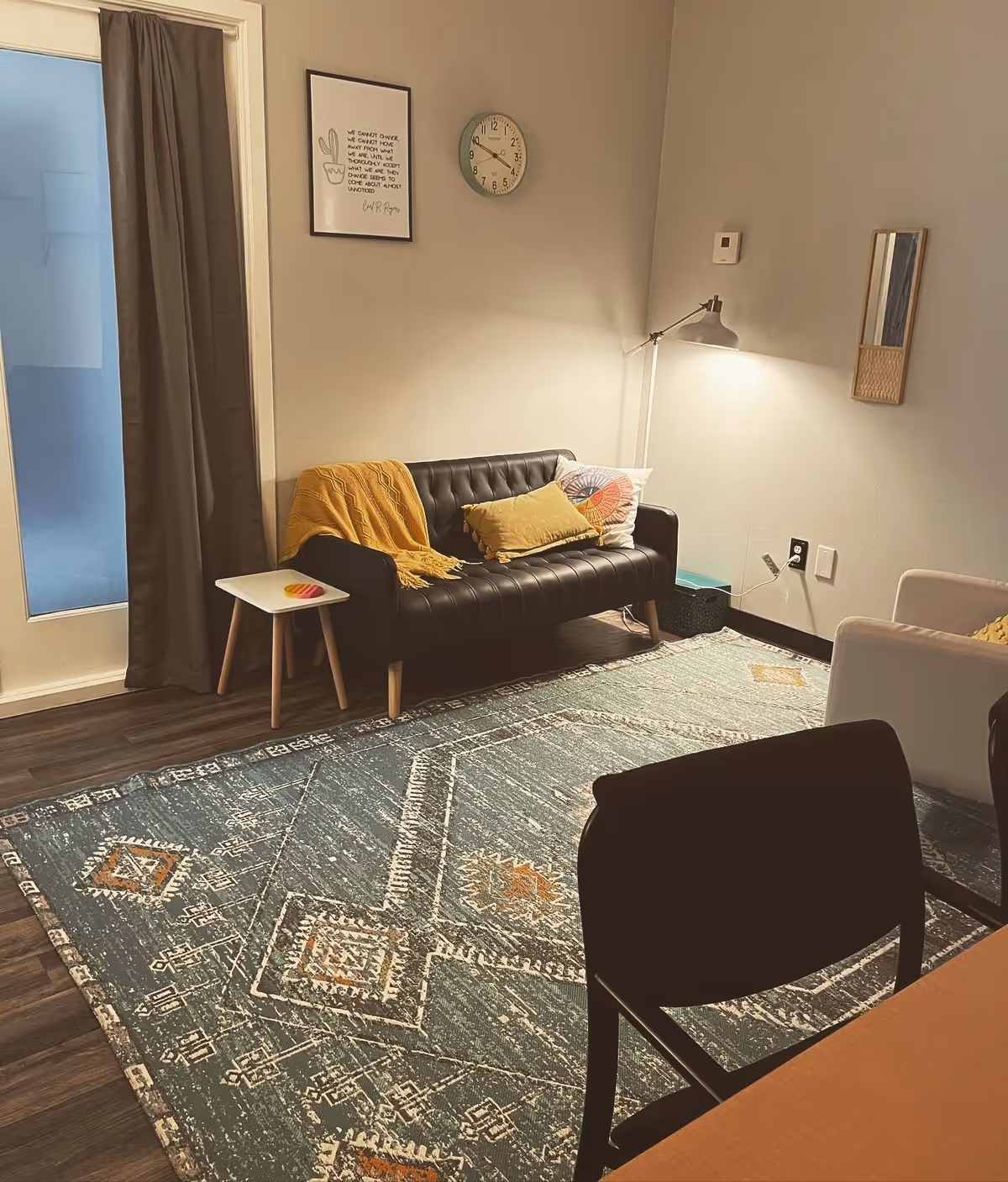Cozy living room in a senior facility with a black tufted sofa, rug, and lamp.