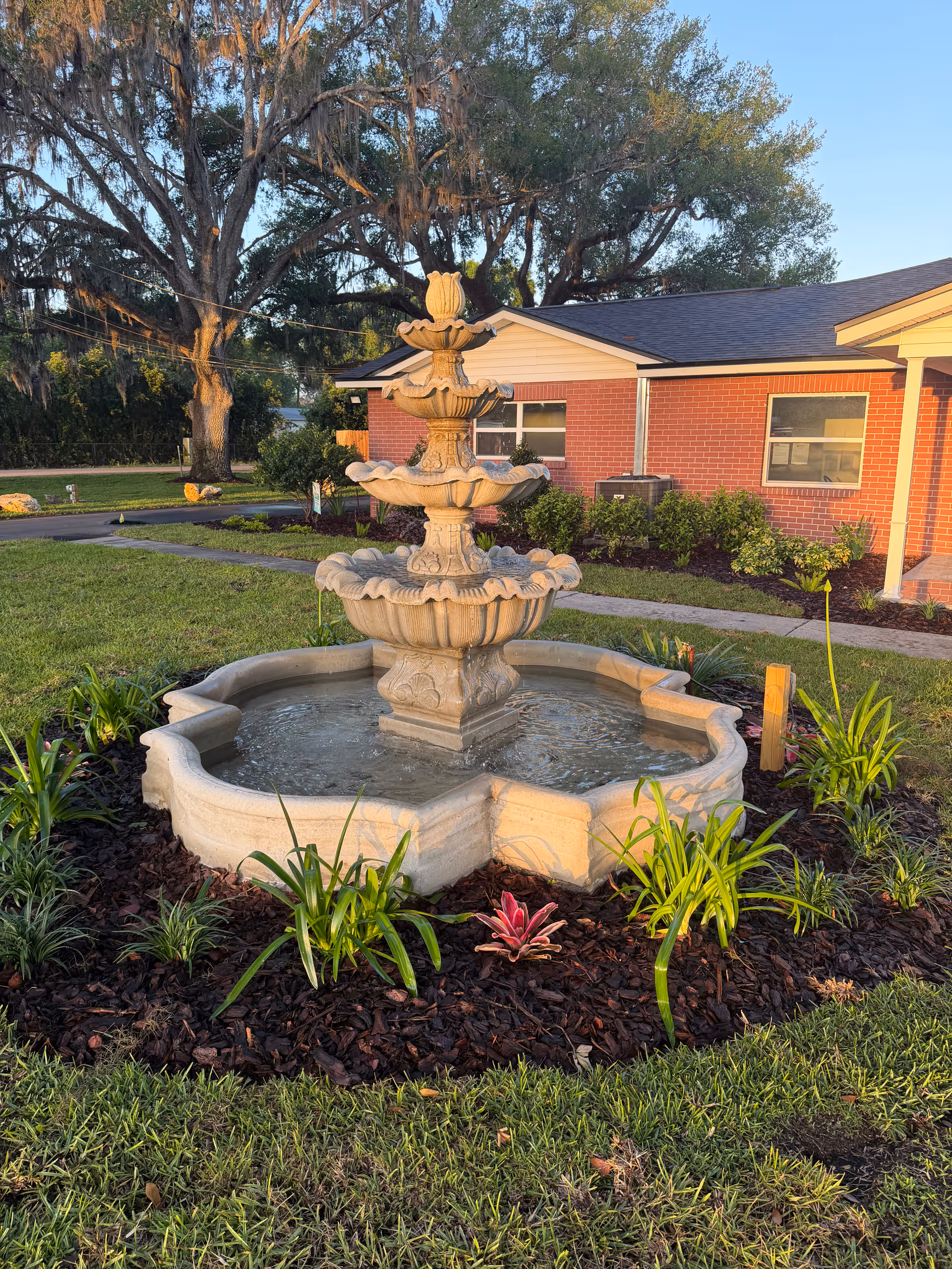 Front view of Heritage Oaks Assisted Living with a tiered fountain and landscaped garden.