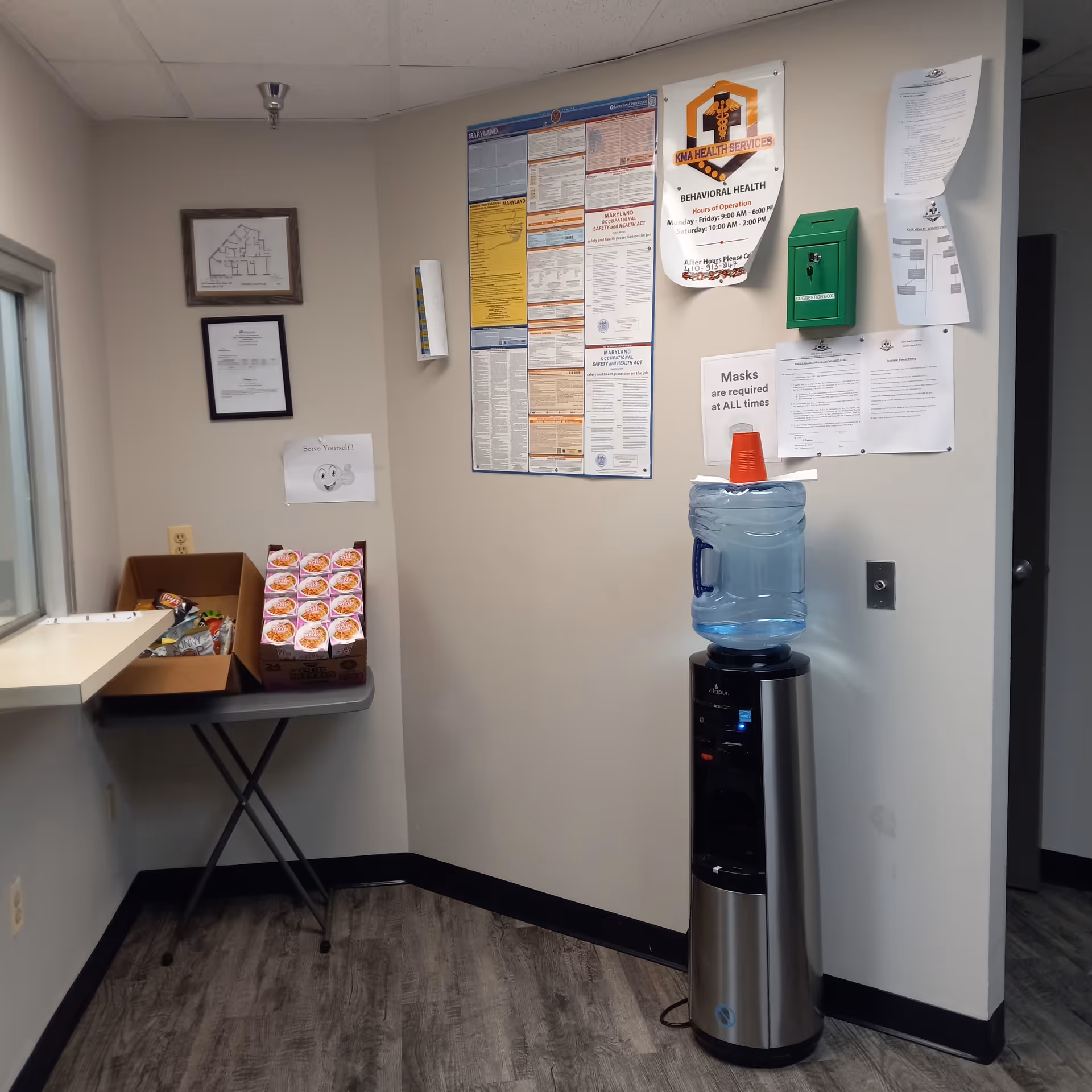 Indoor hallway corner with bulletin boards, water cooler, and snack table.