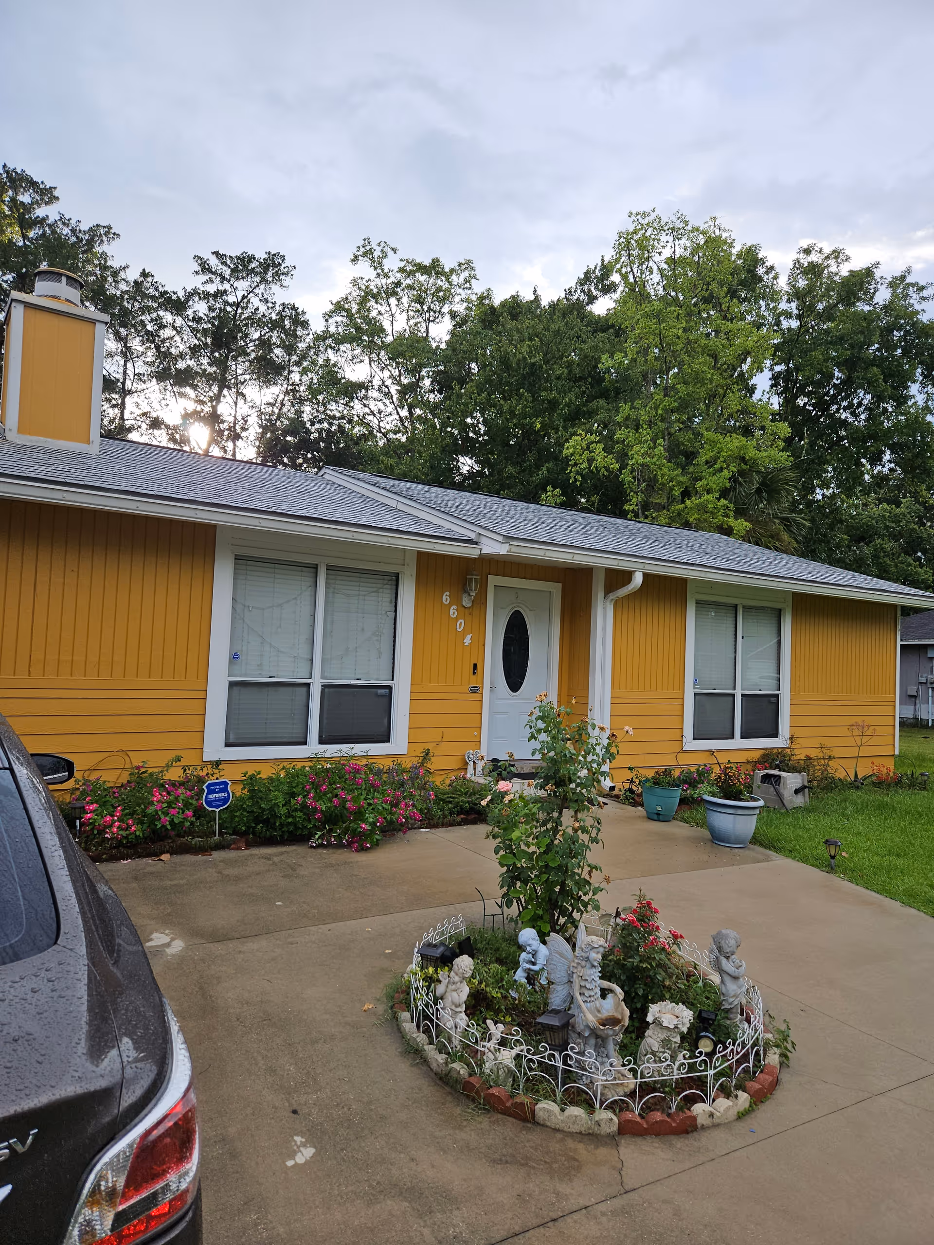 Yellow single-story building with front entrance, flower garden, and decorative statue circle.