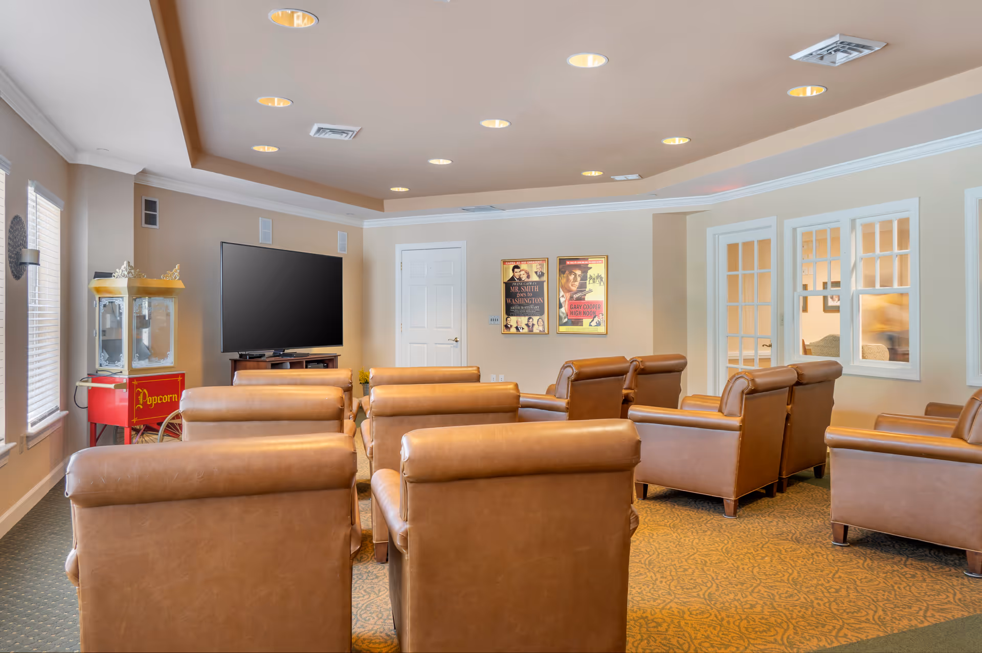 A spacious living room with brown leather lounge chairs, a wall-mounted TV, and posters.