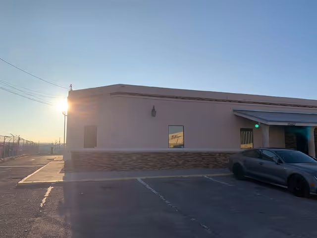 Exterior view of a single-story facility with a parking lot and setting sun.