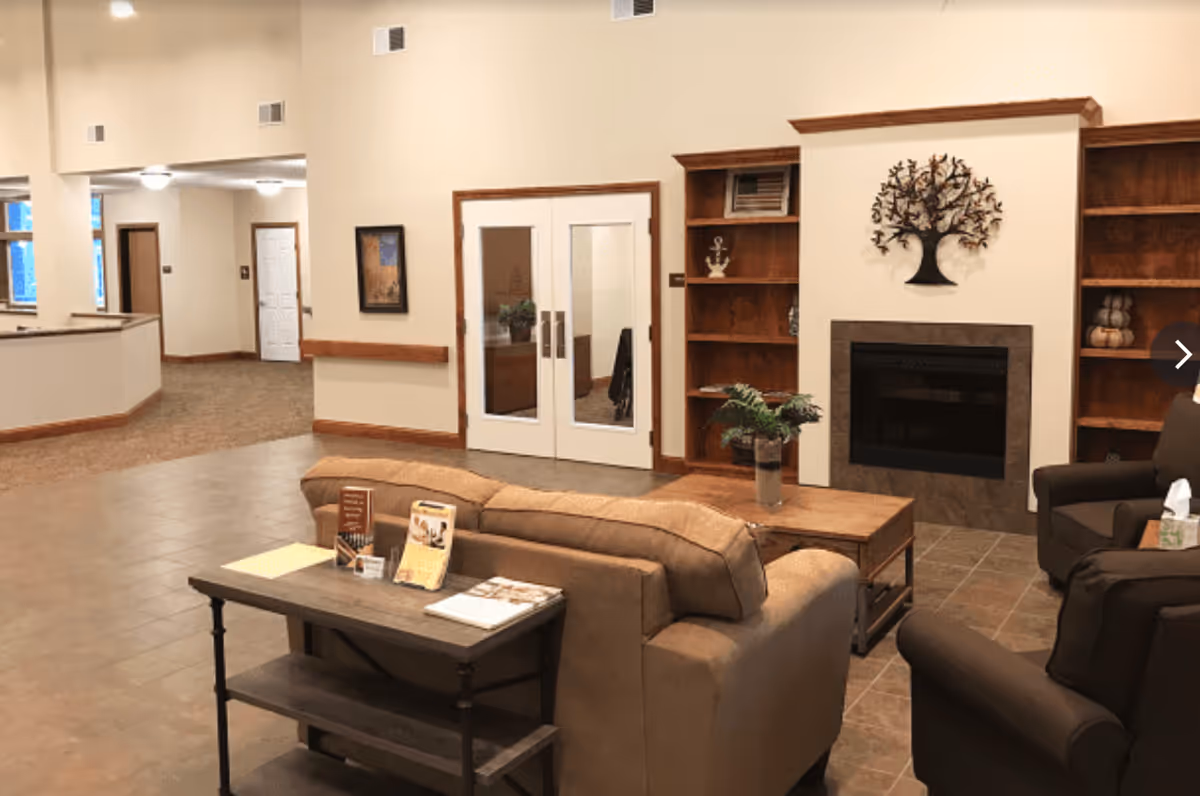 Spacious senior living common area with sofas, armchairs, a fireplace, built-in wooden shelves and double doors.