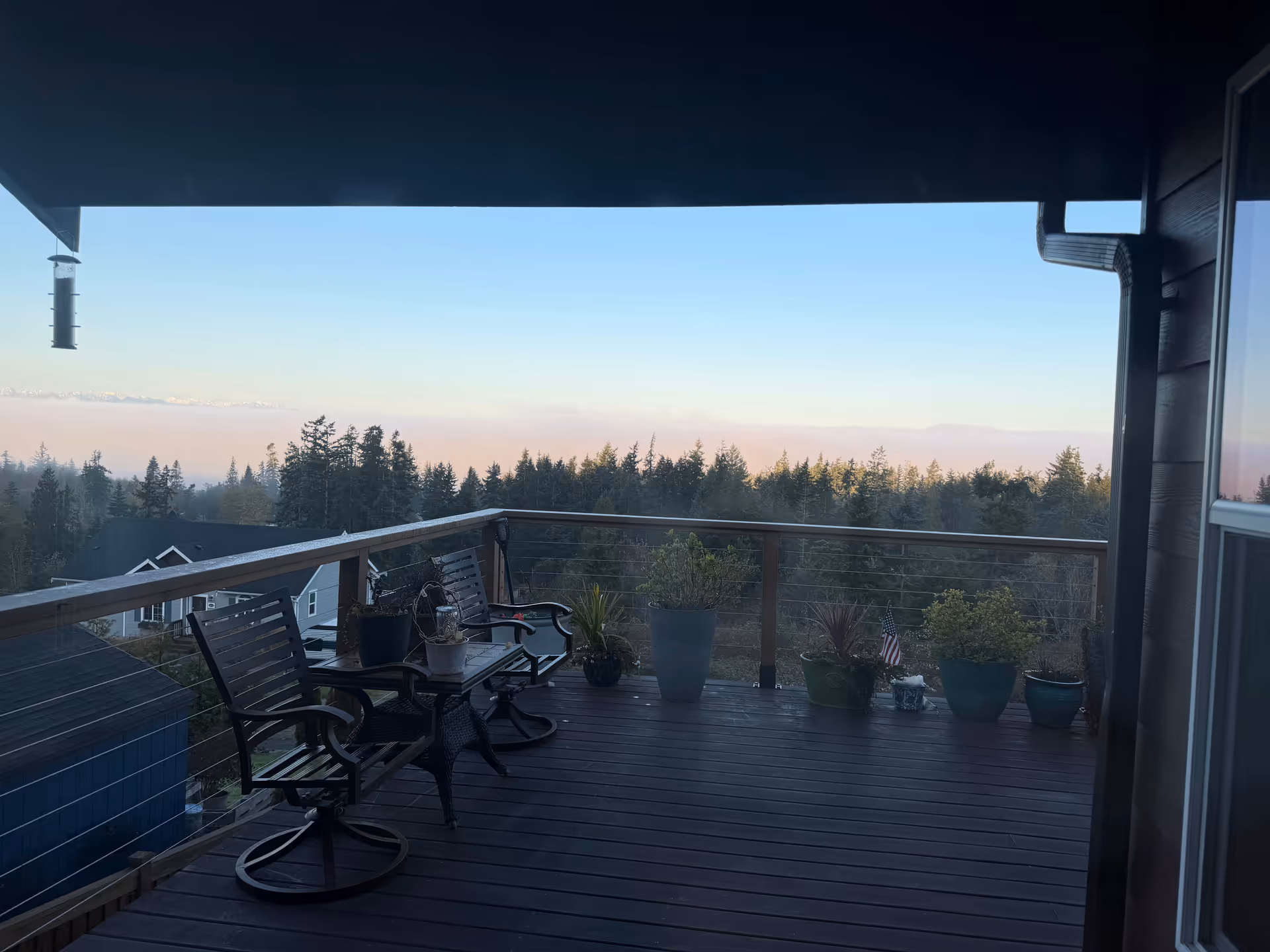 A spacious balcony deck with chairs and potted plants overlooking a forested view.