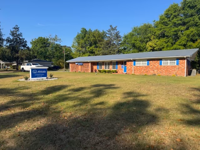 Front view of a single-story brick building with blue doors and a grassy lawn sign.