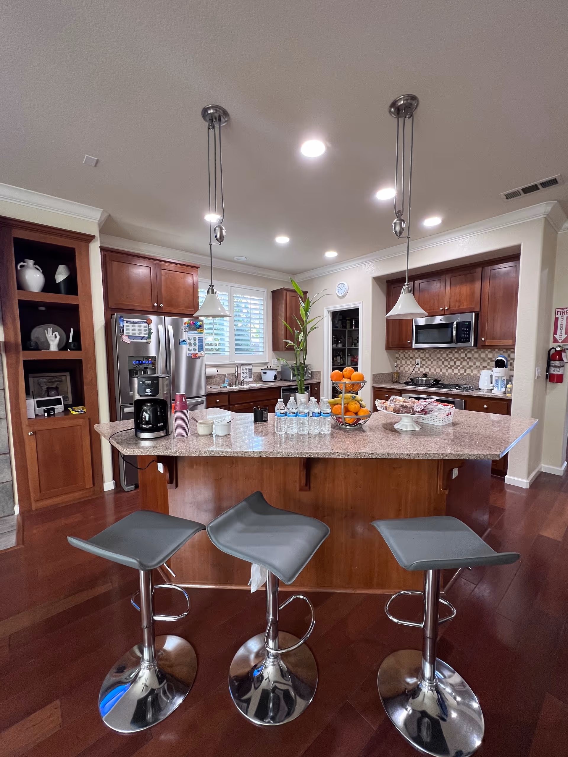 Modern kitchen with island, three stools, and stainless steel appliances.
