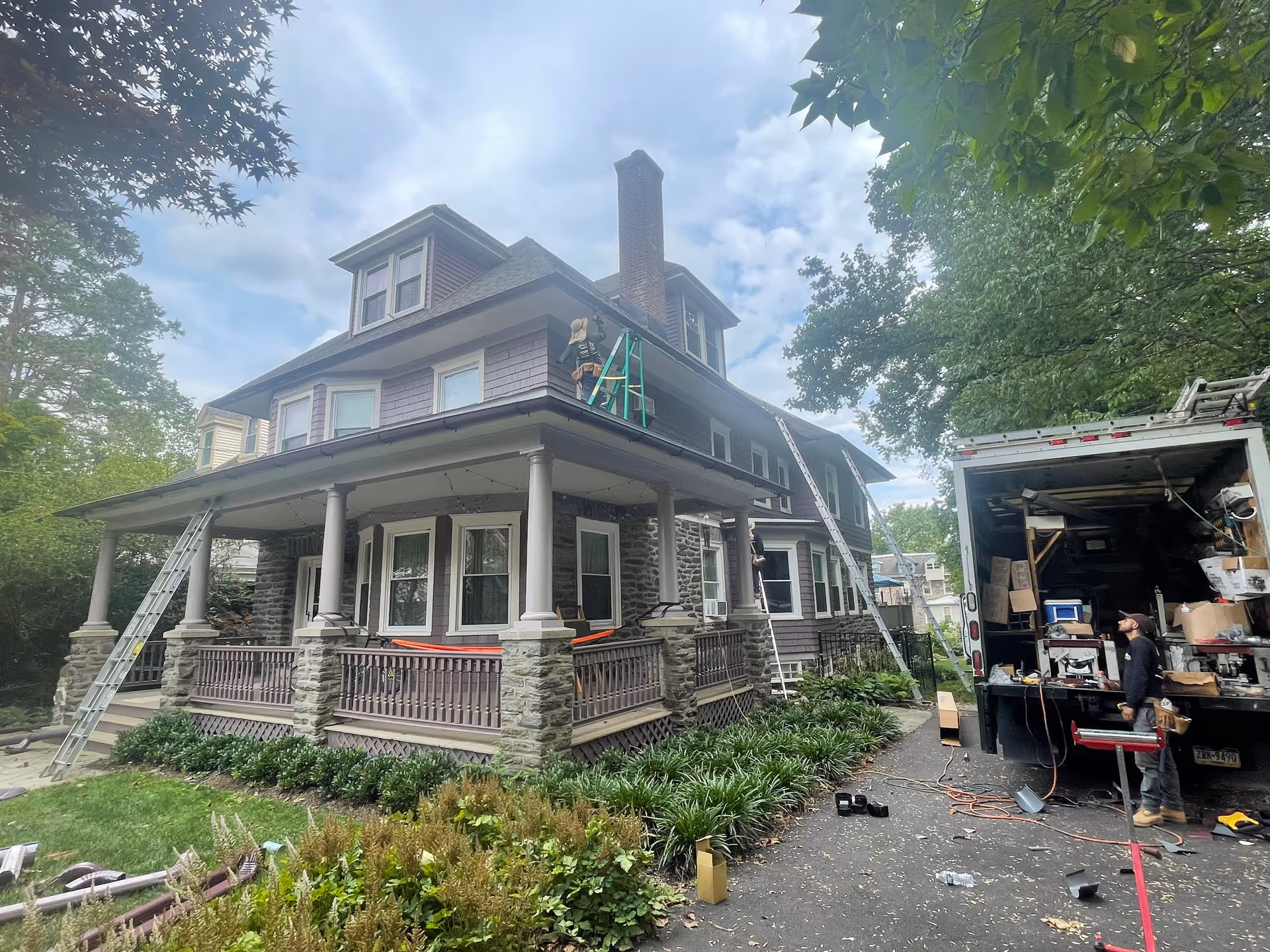 Two-story craftsman-style building under exterior renovation with workers on ladders beside a service truck.