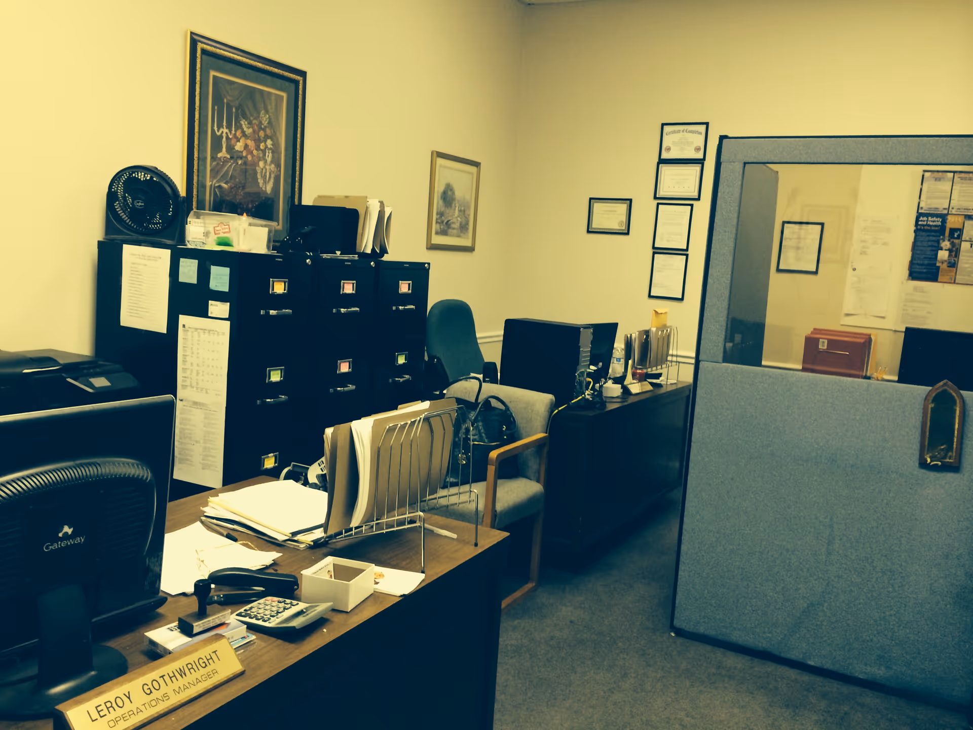 Office workspace with desks, filing cabinets, and framed certificates in a reception area.
