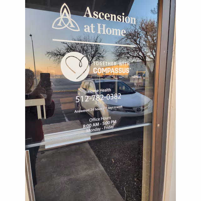 Glass door displays Ascension at Home branding and contact info, reflecting a car outside.