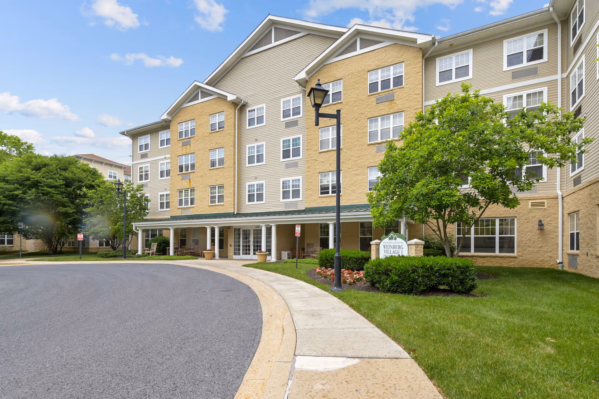 Exterior view of a multi-story senior living building with a curved driveway and landscaped entrance
