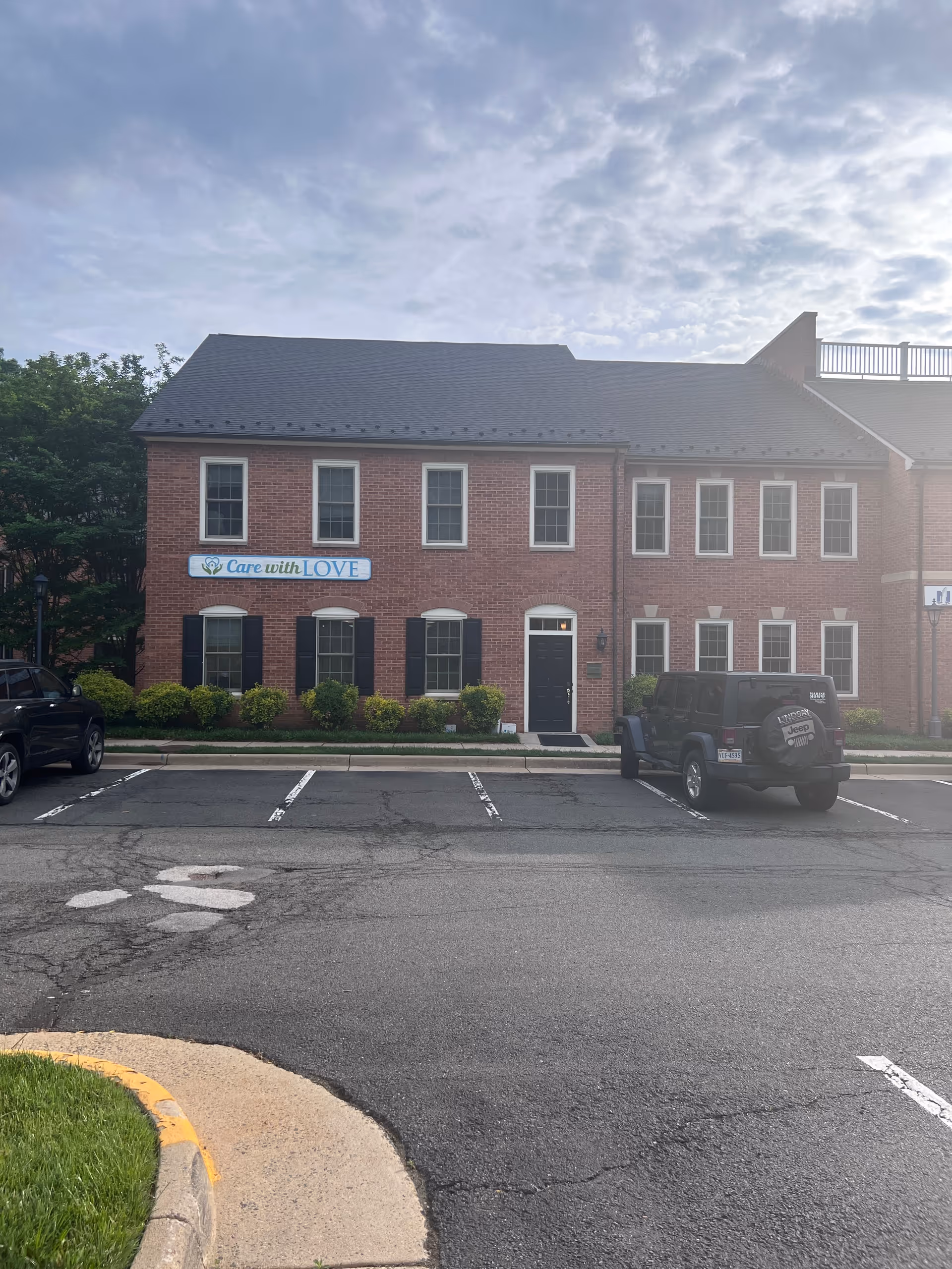 Brick senior living facility with Care with LOVE sign and parked cars in front.