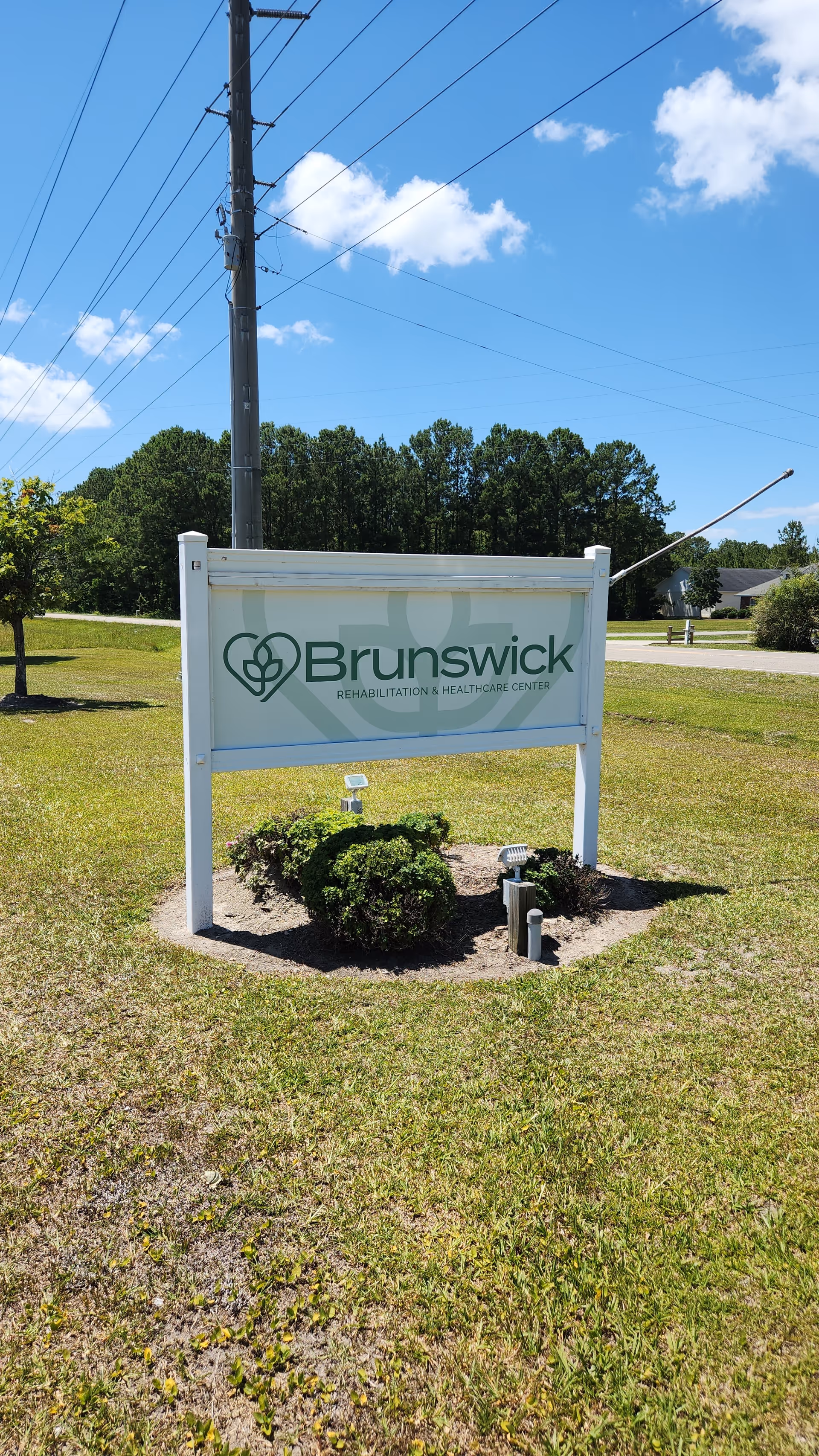 Outdoor sign for Brunswick Rehabilitation & Healthcare Center on a grassy lawn with trees and power lines in the background.