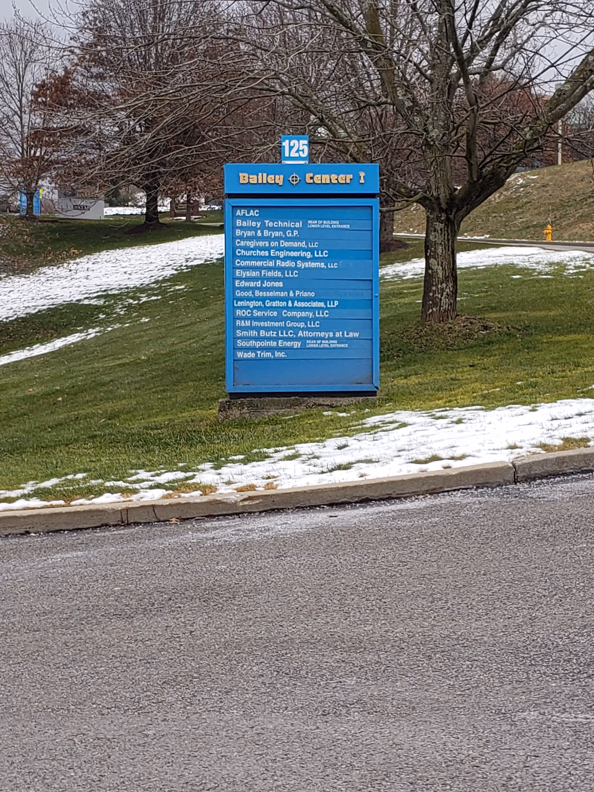 Blue outdoor signboard listing tenants for Bailey Center I on a snowy lawn.