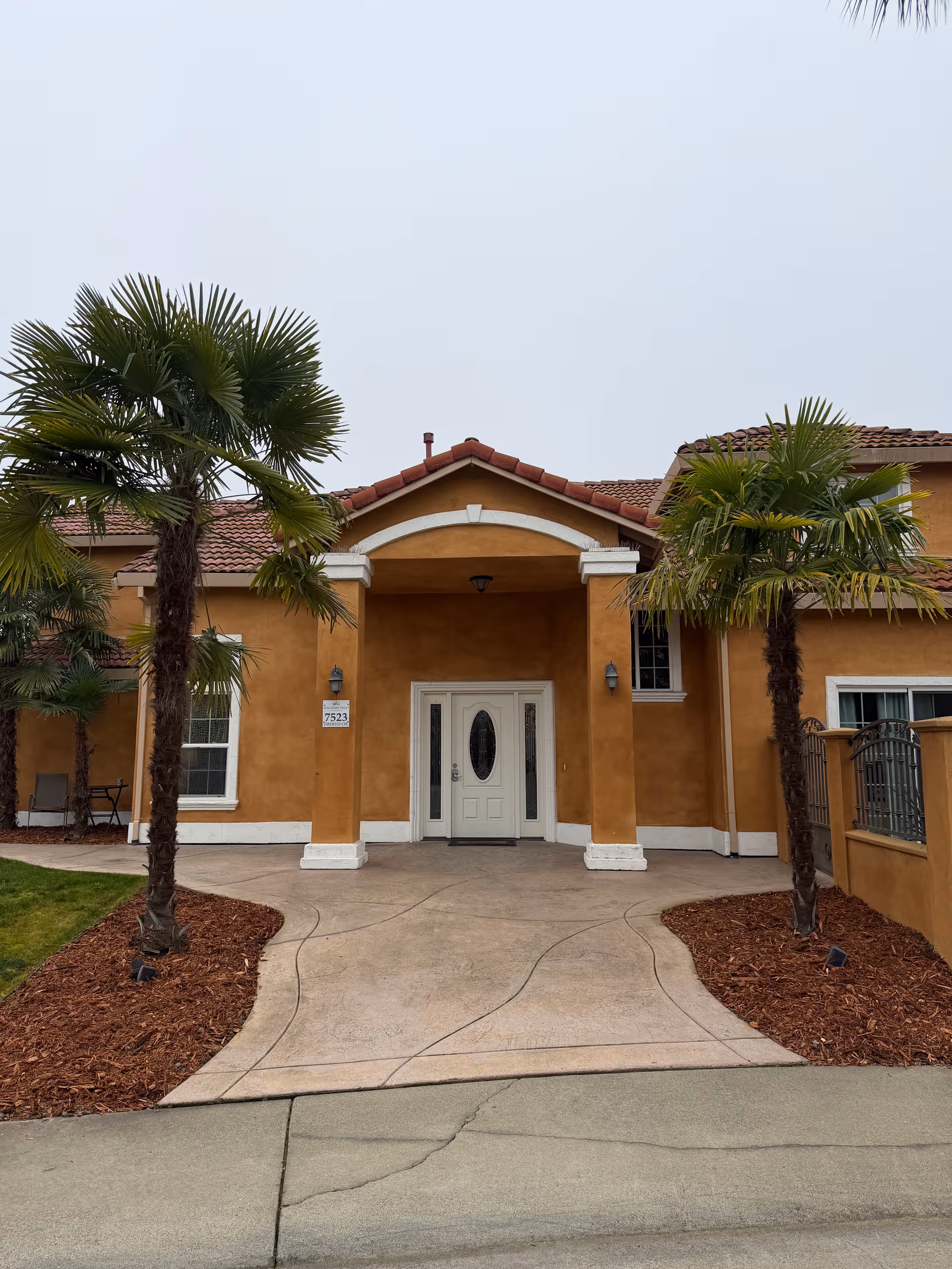 Sunlit beige senior living facility with arched entry, palm trees, and a curved walkway.