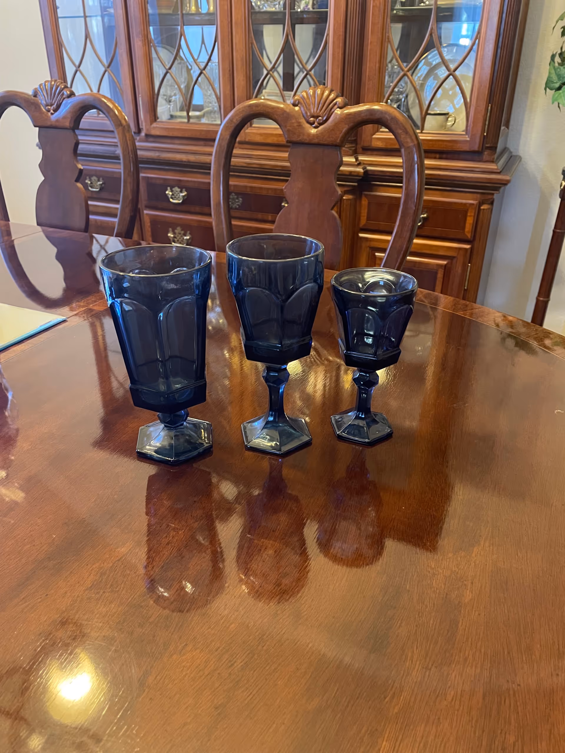Three dark blue goblets arranged on a polished wooden dining table.