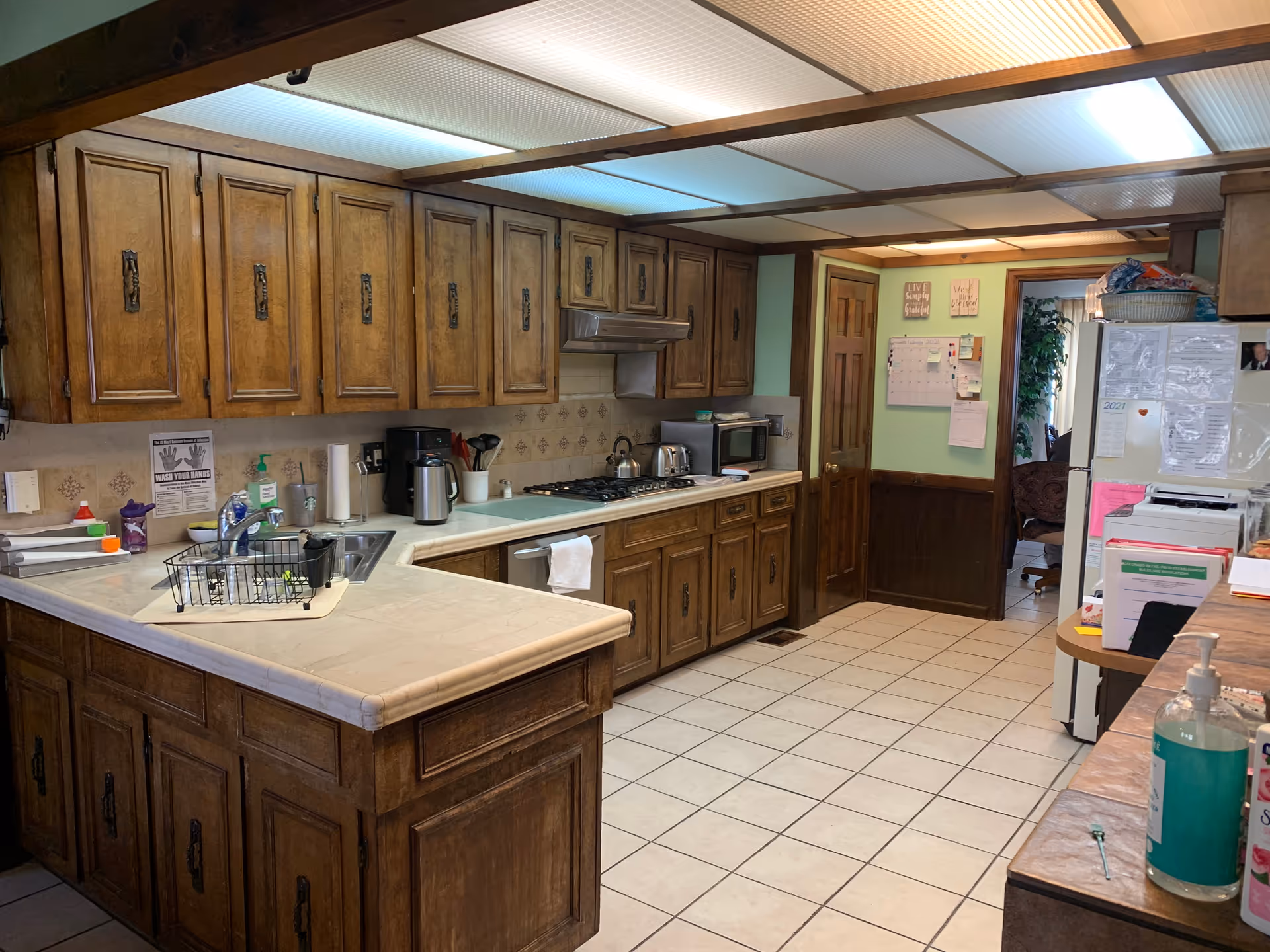 Spacious wooden kitchen with upper cabinets, appliances, and a refrigerator in a senior living facility.
