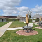 Sunlit outdoor courtyard with round table, chairs, umbrellas, and green lawns