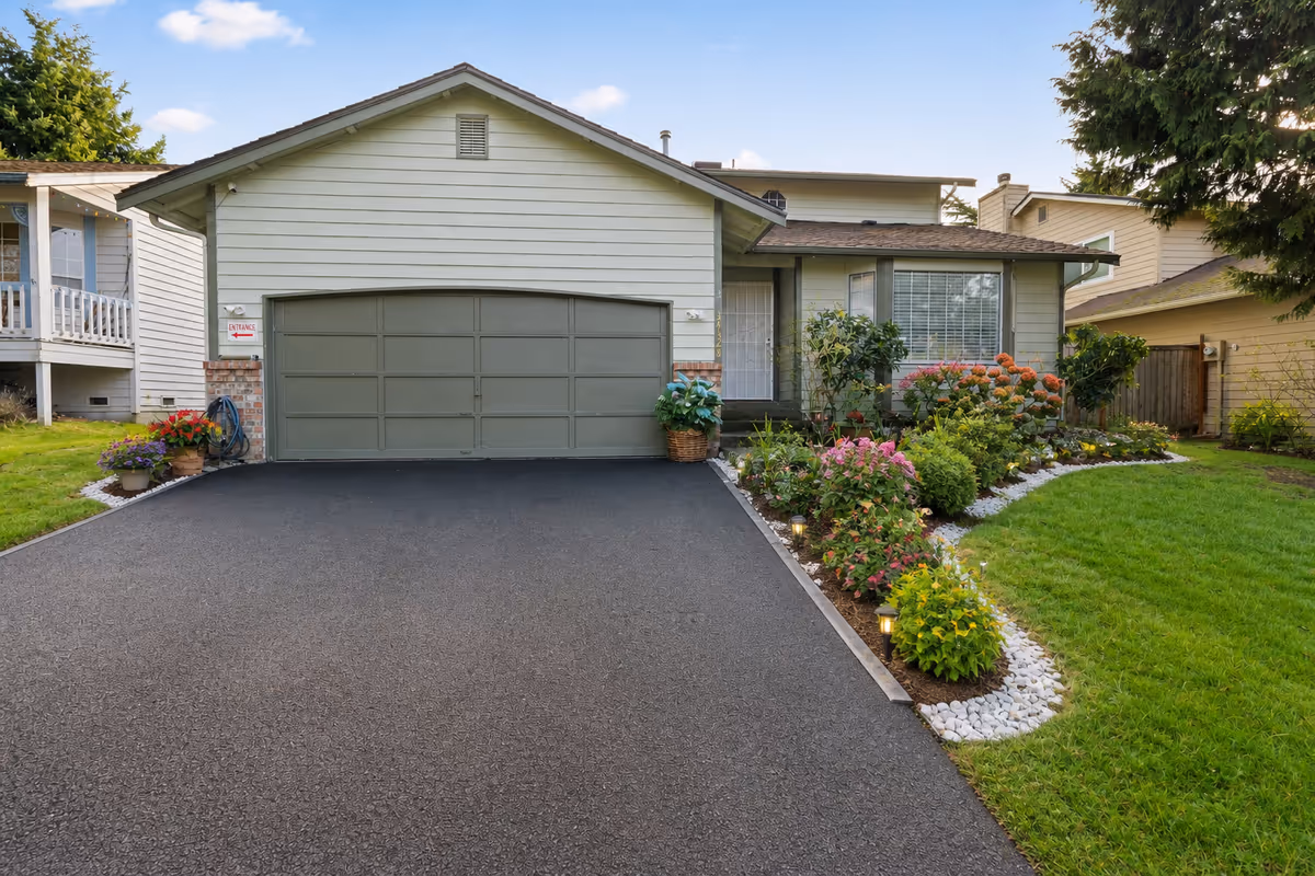 Front exterior of a light green, single-story home with a two-car garage and landscaped yard.