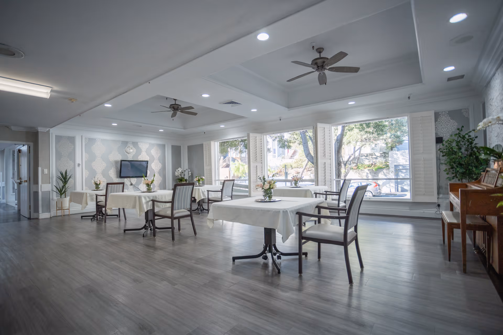 Bright senior living dining area with tables, chairs, and large windows.