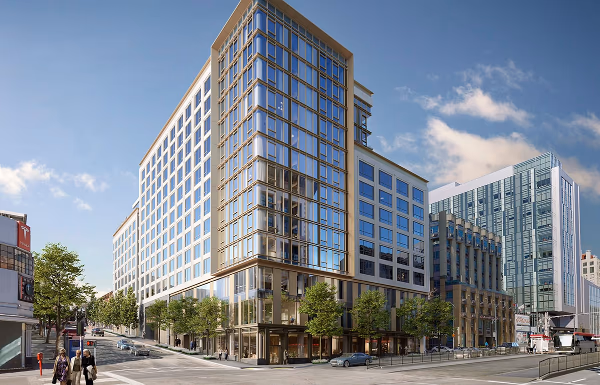 Modern multi-story glass-front building at a city street corner with trees, cars, and pedestrians.