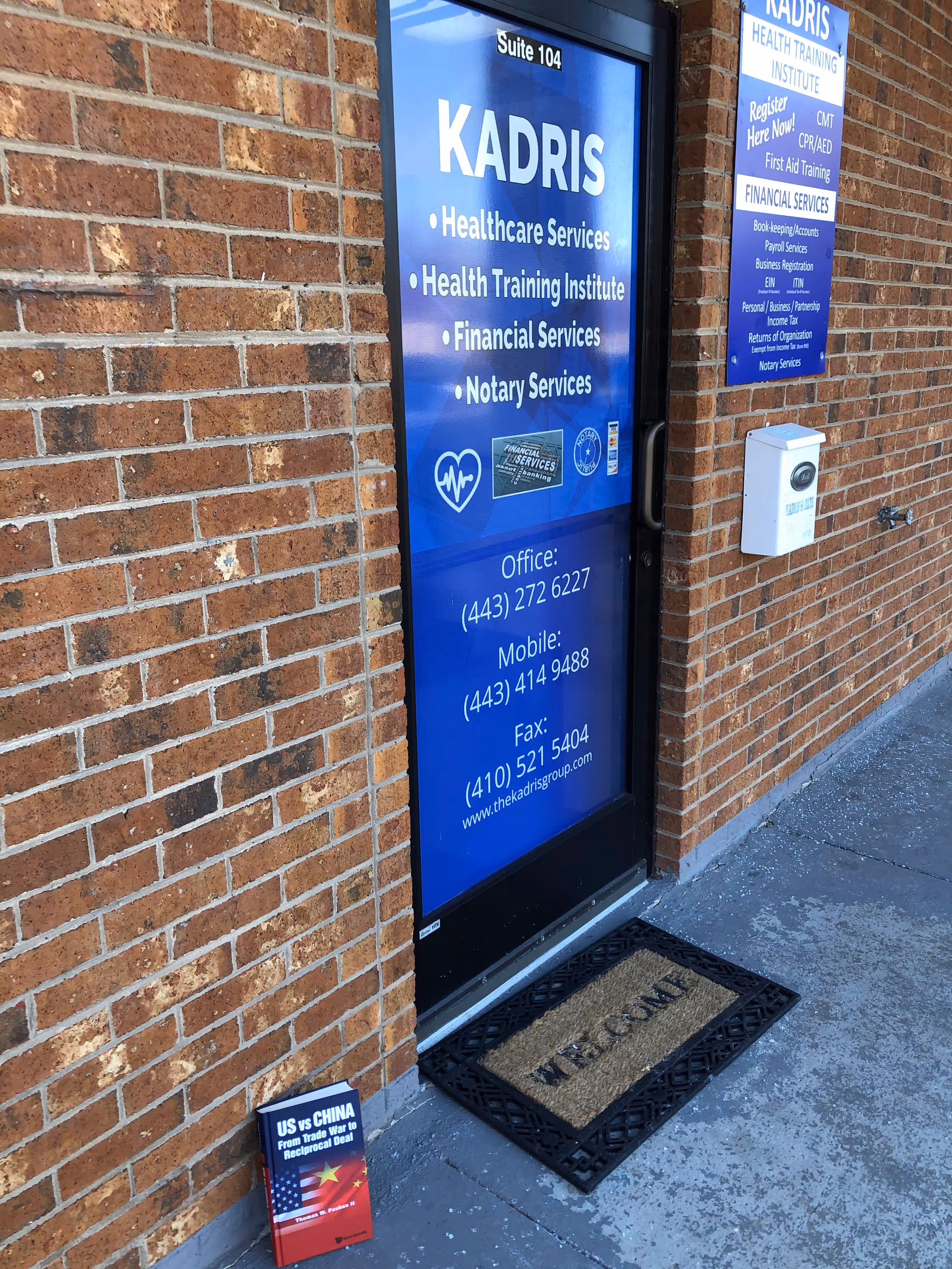 Blue sign on brick exterior door for Kadris Healthcare Services and contact numbers.