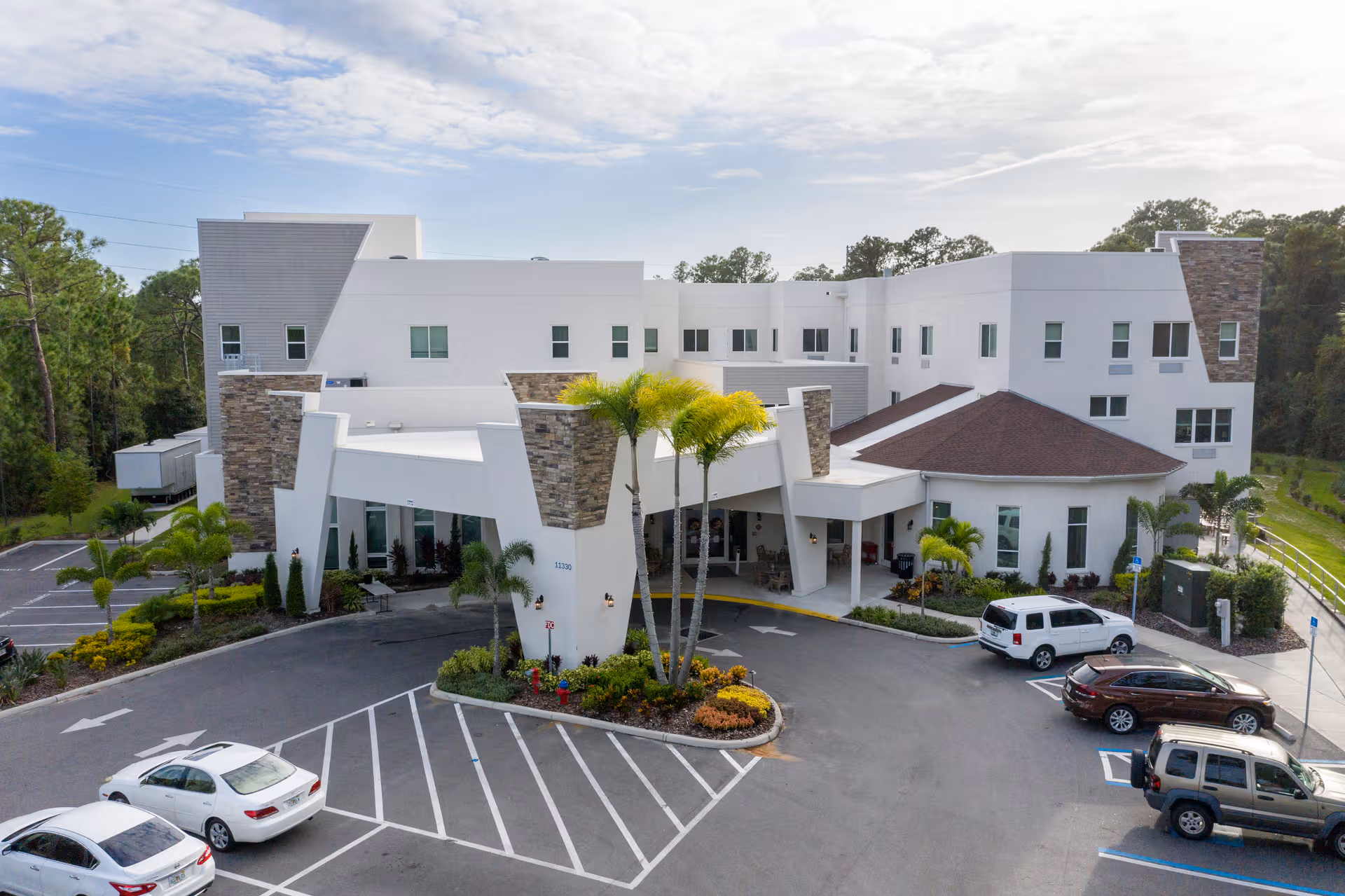 Modern white senior living facility with parking lot and landscaped entry plaza.