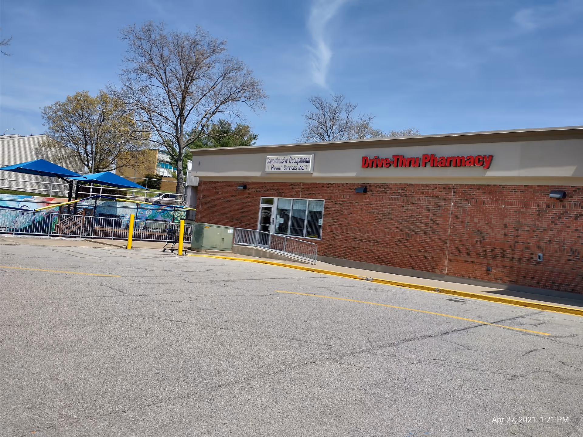 Exterior view of a brick building with a Drive-Thru Pharmacy sign and blue umbrellas.