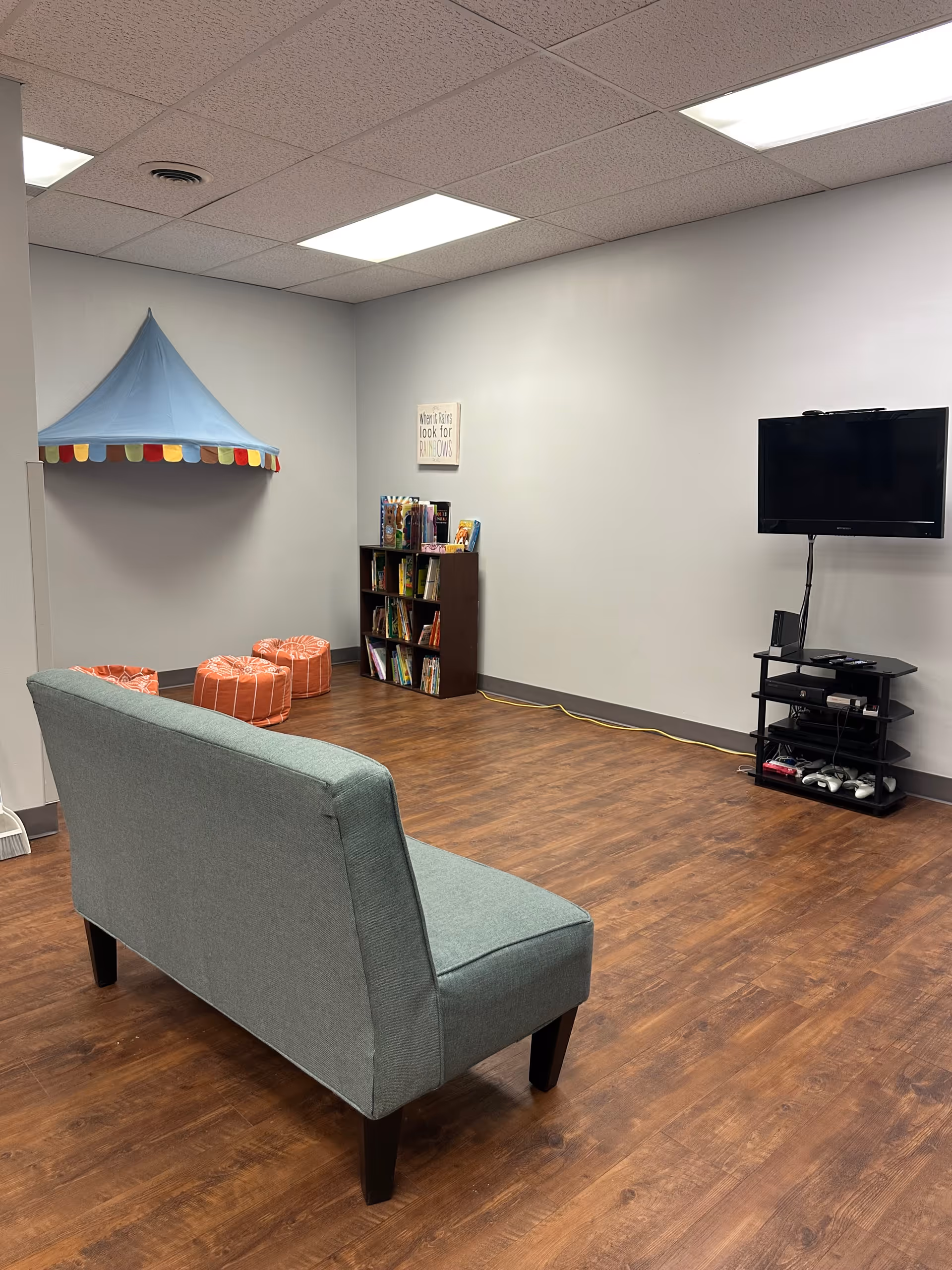 A lounge area with a teal sofa, wooden floor, TV, bookshelf, and a blue tent canopy.
