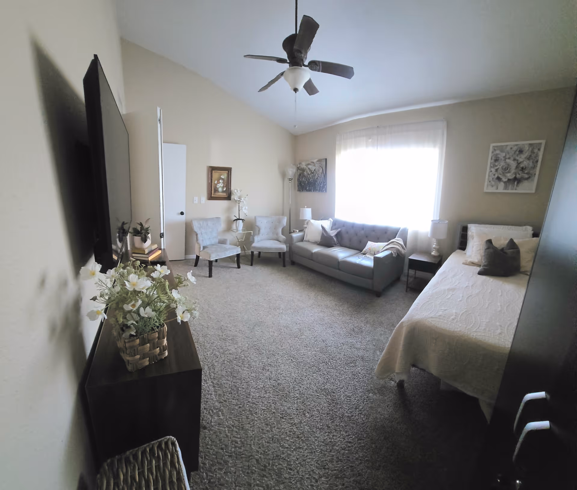 Senior living suite with bed, sofa, chairs, TV and a large window.