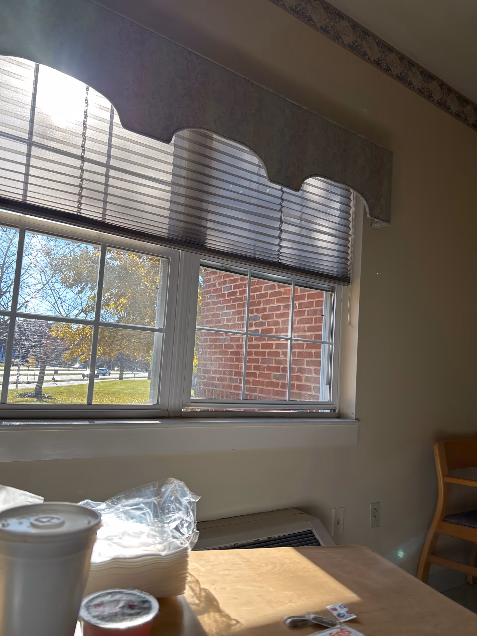 Interior dining area with a window, blinds, a wooden table, disposable cup, and chairs.