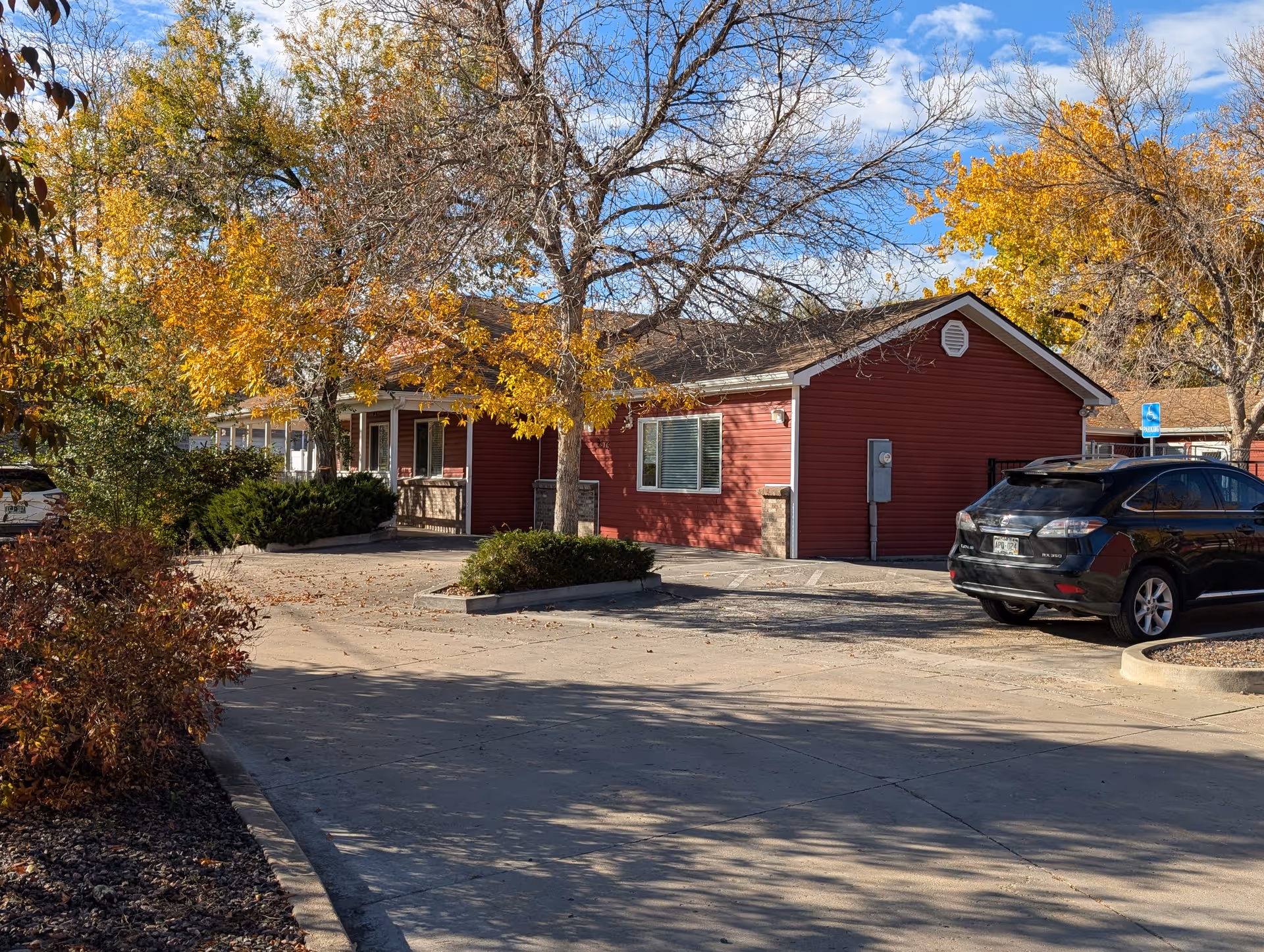 Red single-story assisted living building with parking and autumn trees