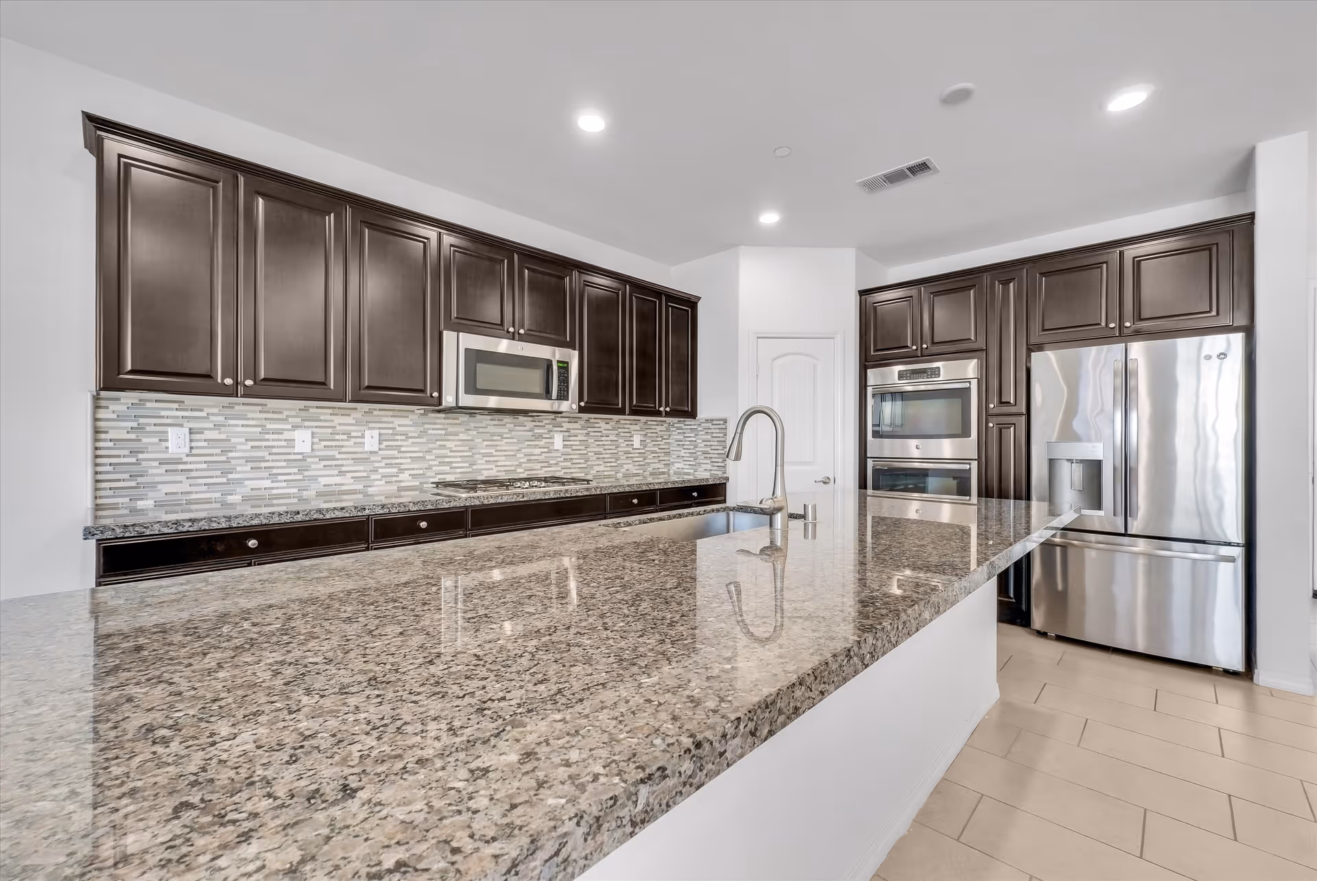 Modern kitchen with granite island, dark cabinetry, and stainless steel appliances.