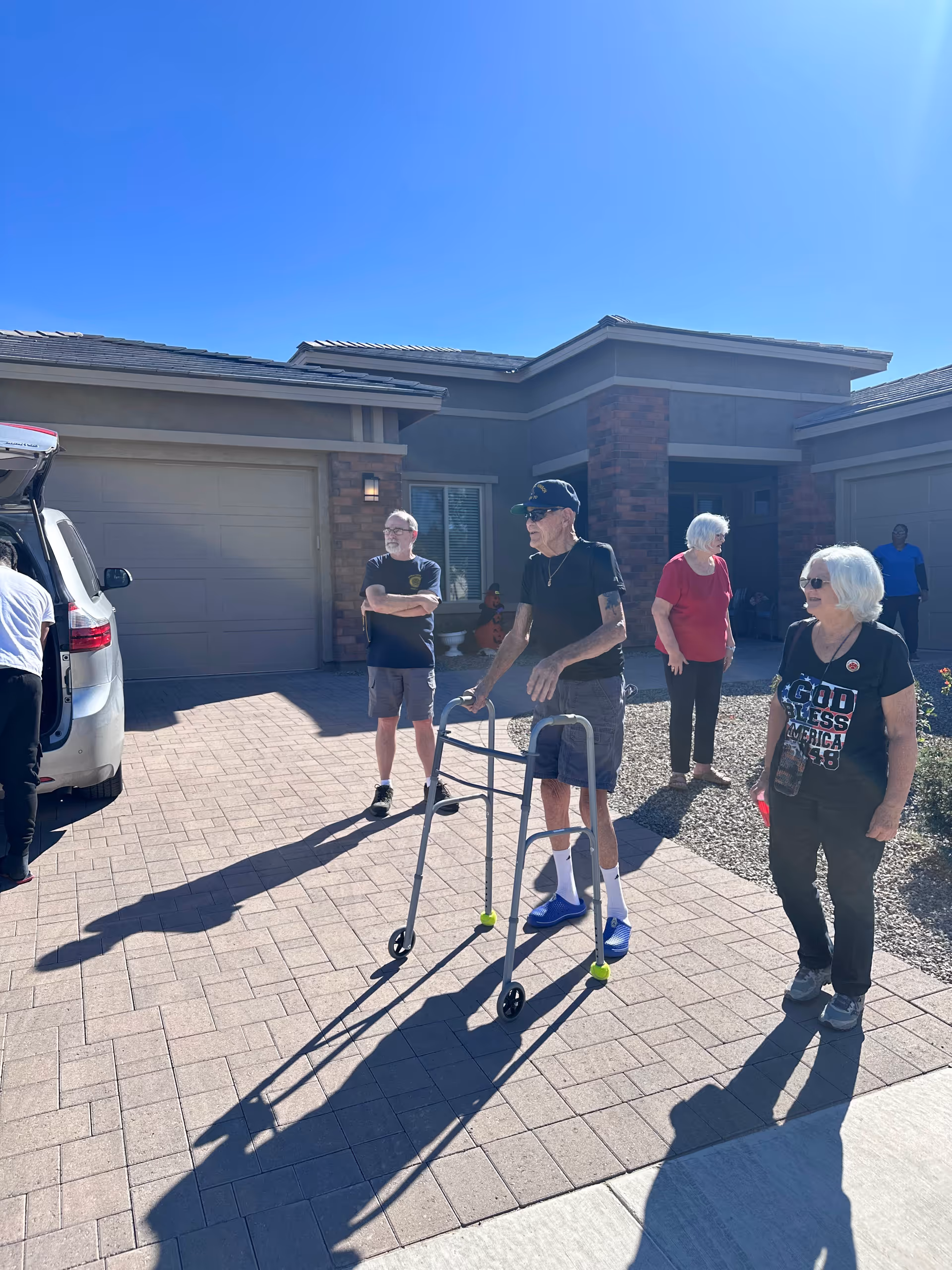Group of seniors outside Harvest at Queen Creek Assisted Living, with a walker on brick driveway