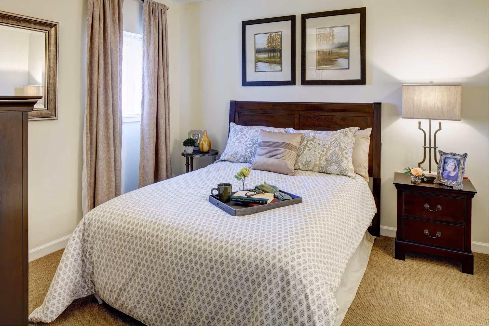 Neatly made bedroom with a wooden bed, two nightstands, lamps, and a tray on the bed.