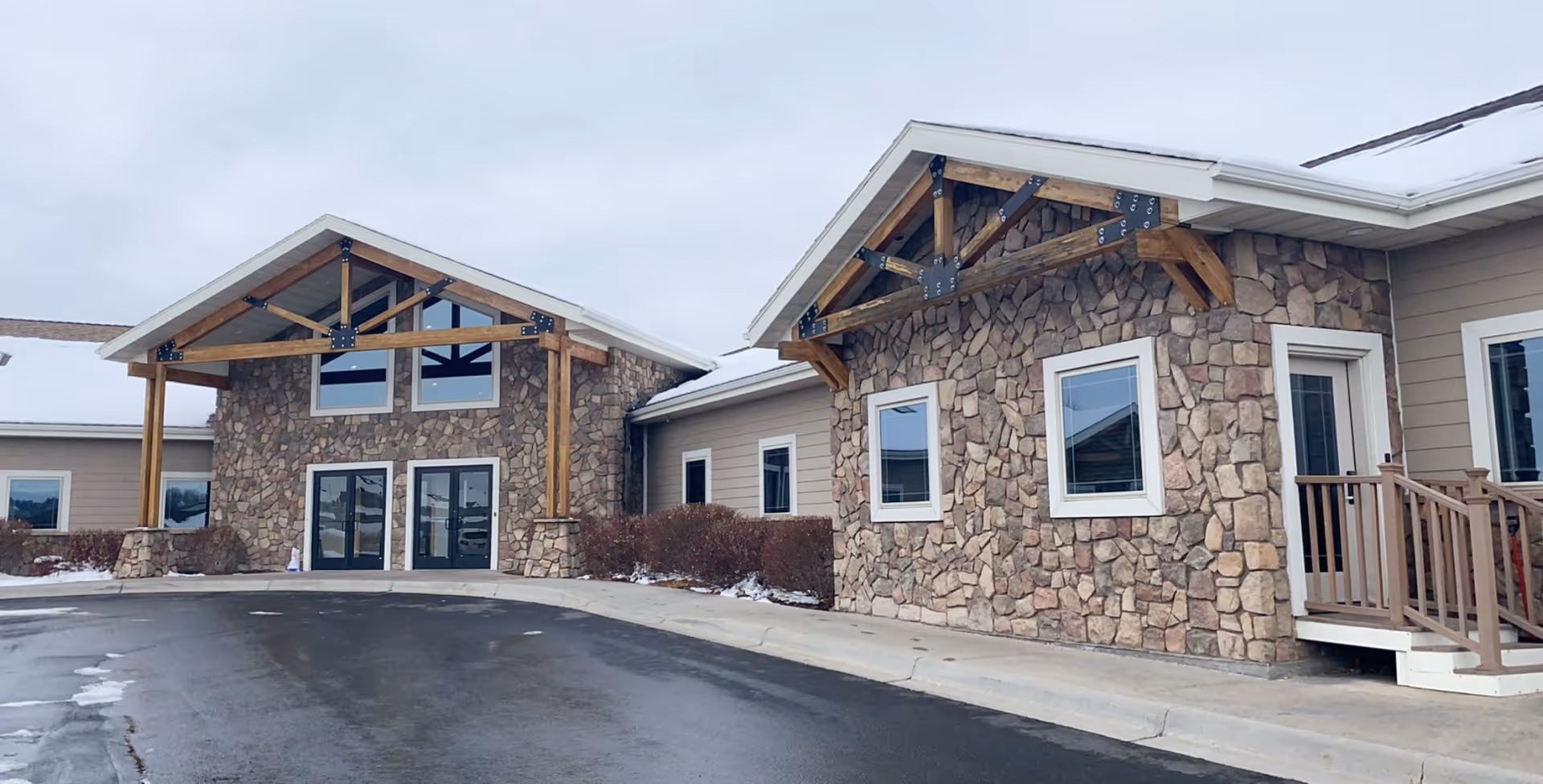 Stone-clad senior living facility exterior with wooden supports and snow along walkway