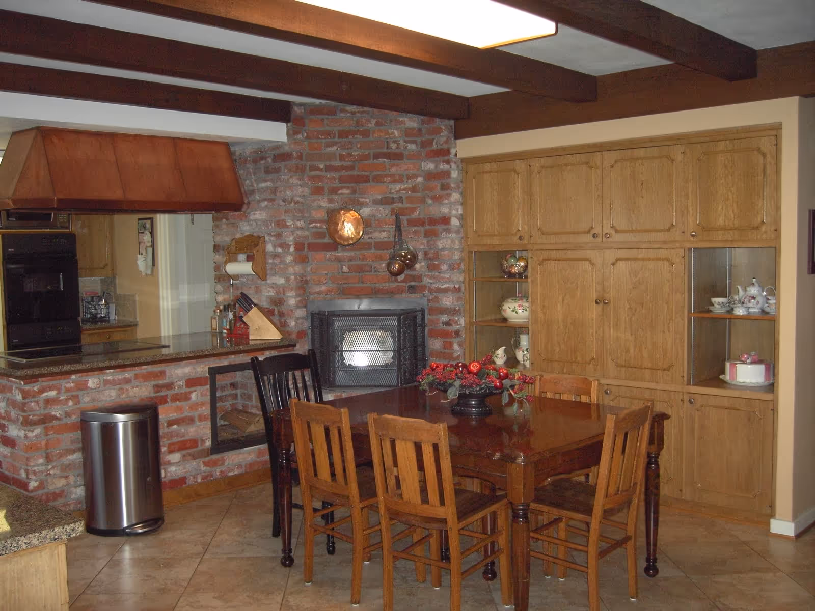 Open dining room with brick fireplace, wooden beams, and built-in cabinets.